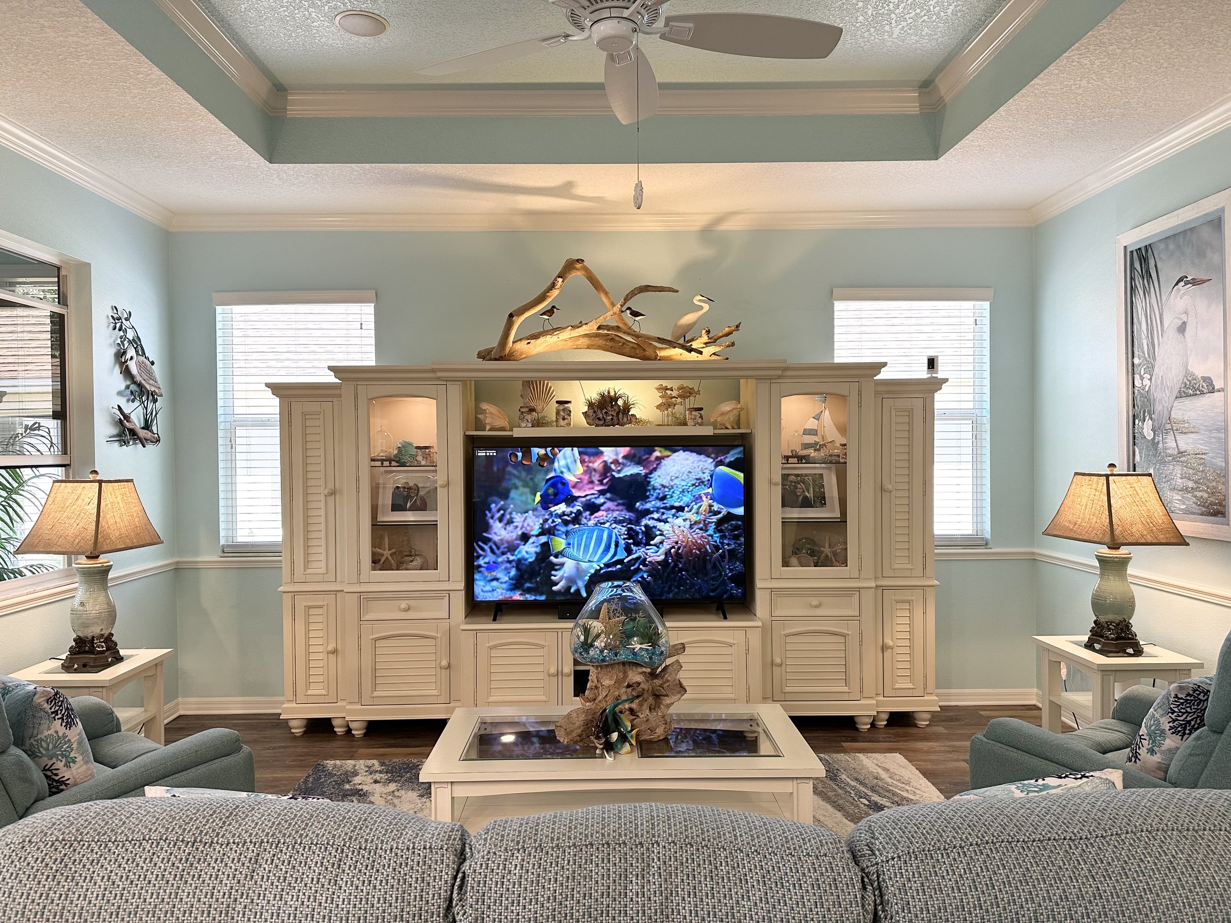 Coastal-themed living room with light blue walls, white entertainment center, decorative elements, and a large TV displaying an ocean scene.