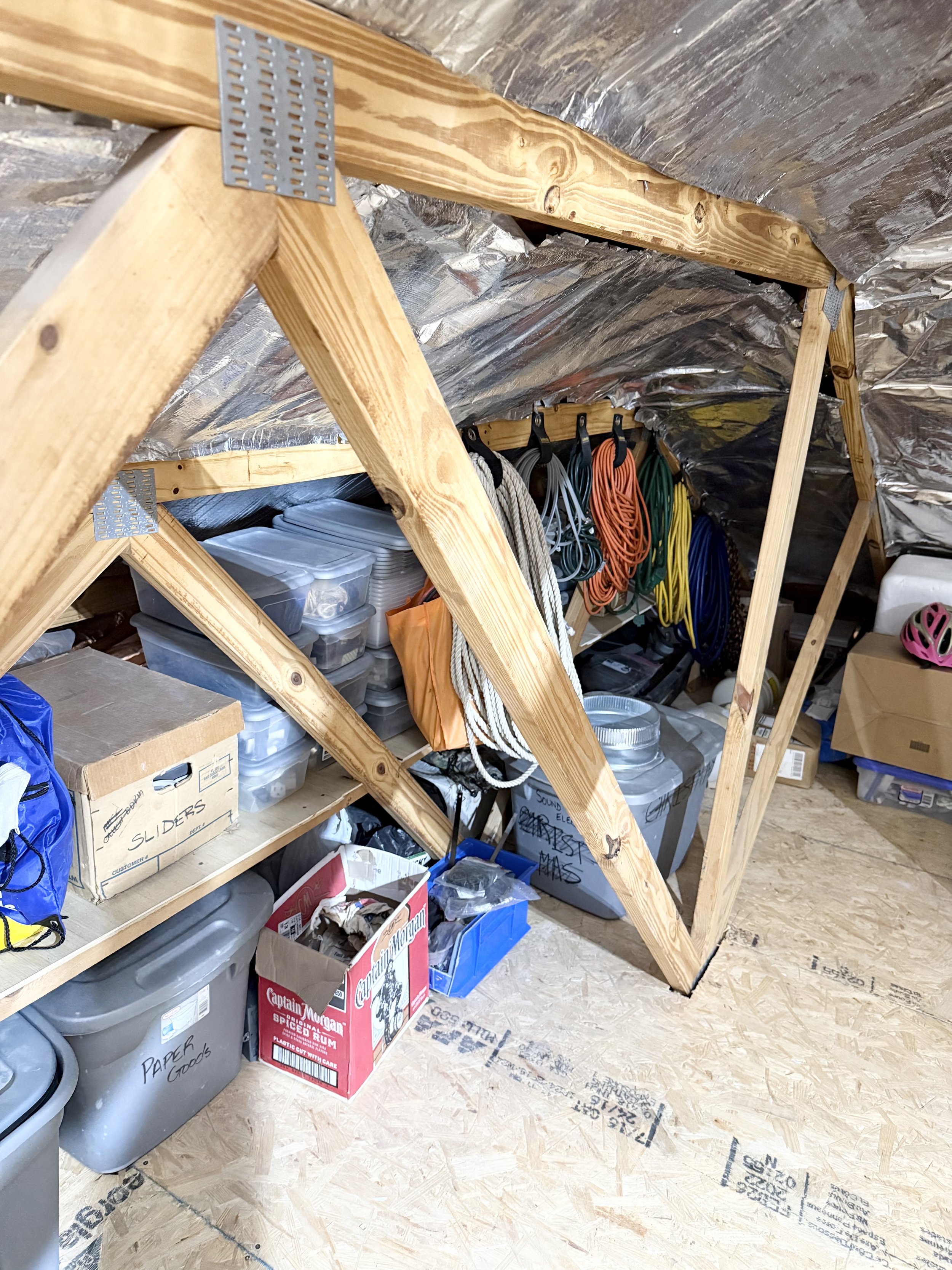 Attic storage space with wooden beams, plastic bins, cardboard boxes, and neatly hung extension cords.
