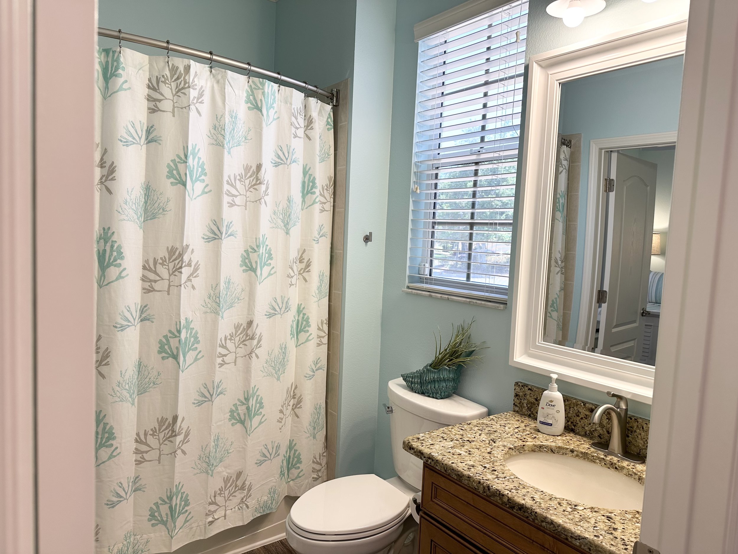 Bathroom with blue walls, floral shower curtain, granite countertop, and decorative plant