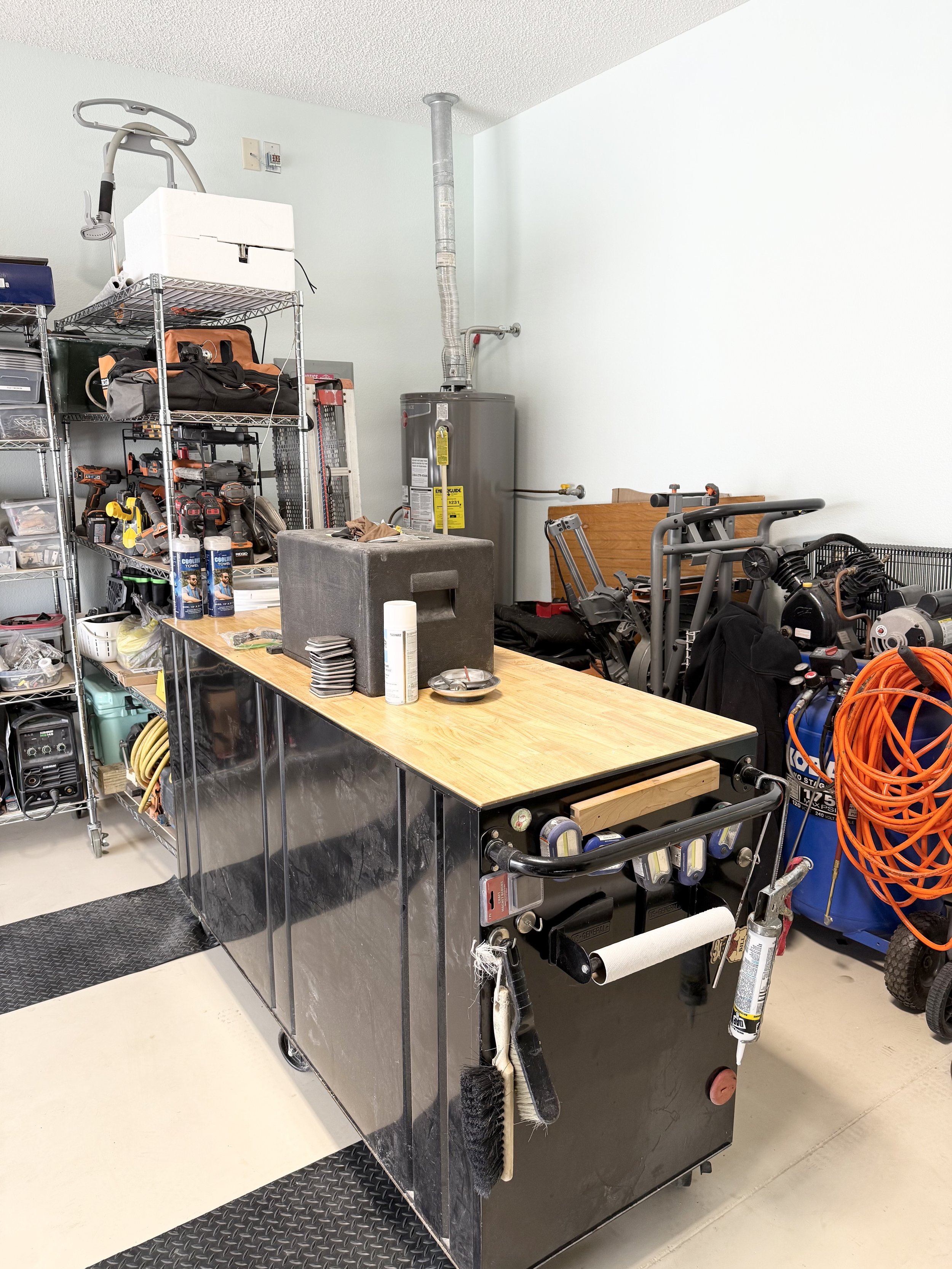 Garage workspace with black tool cabinet, shelving with tools, water heater, and orange extension cords.