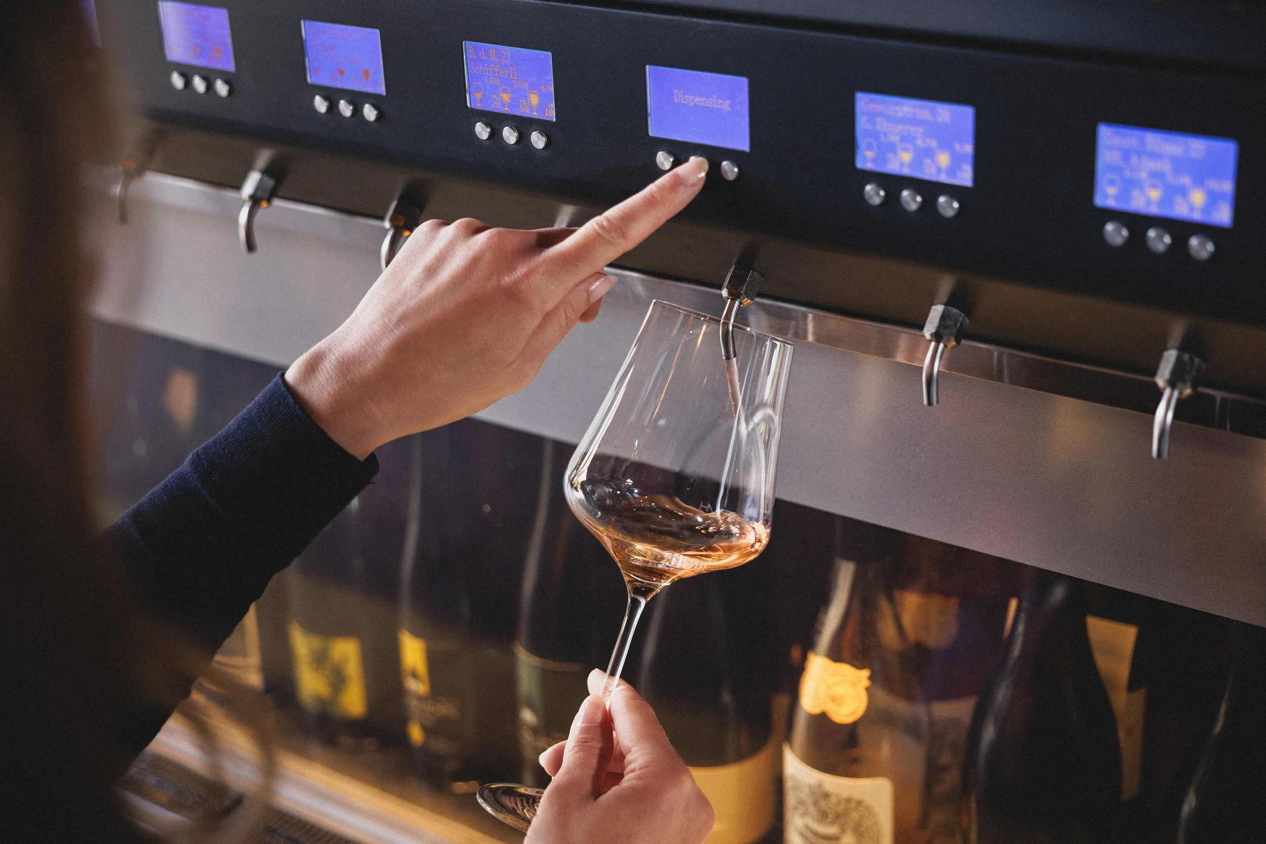Eine Person lässt Wein aus dem Weinautomaten raus.