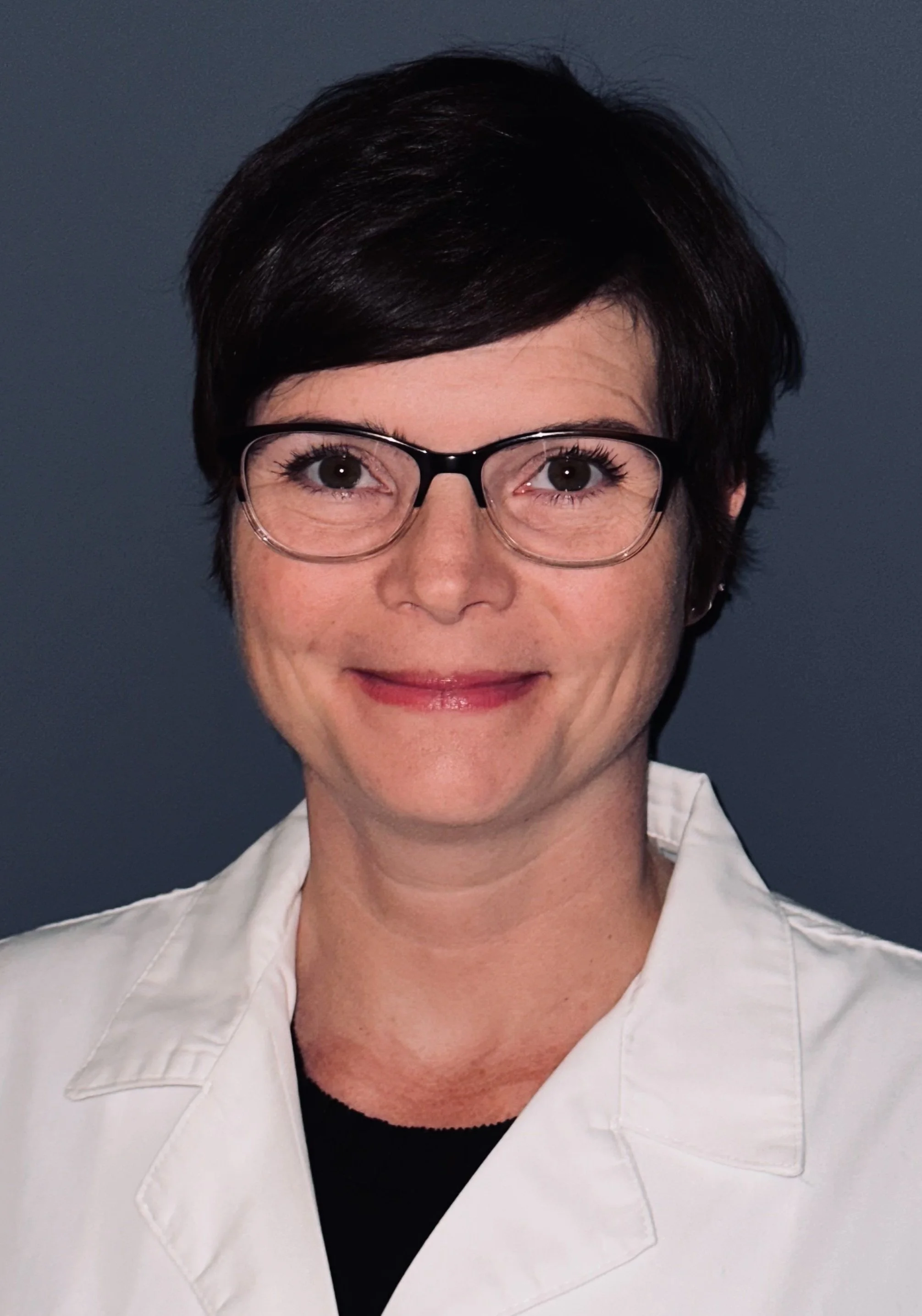 Dr. Alexis Cutchins wearing a white coat, standing against a dark background.