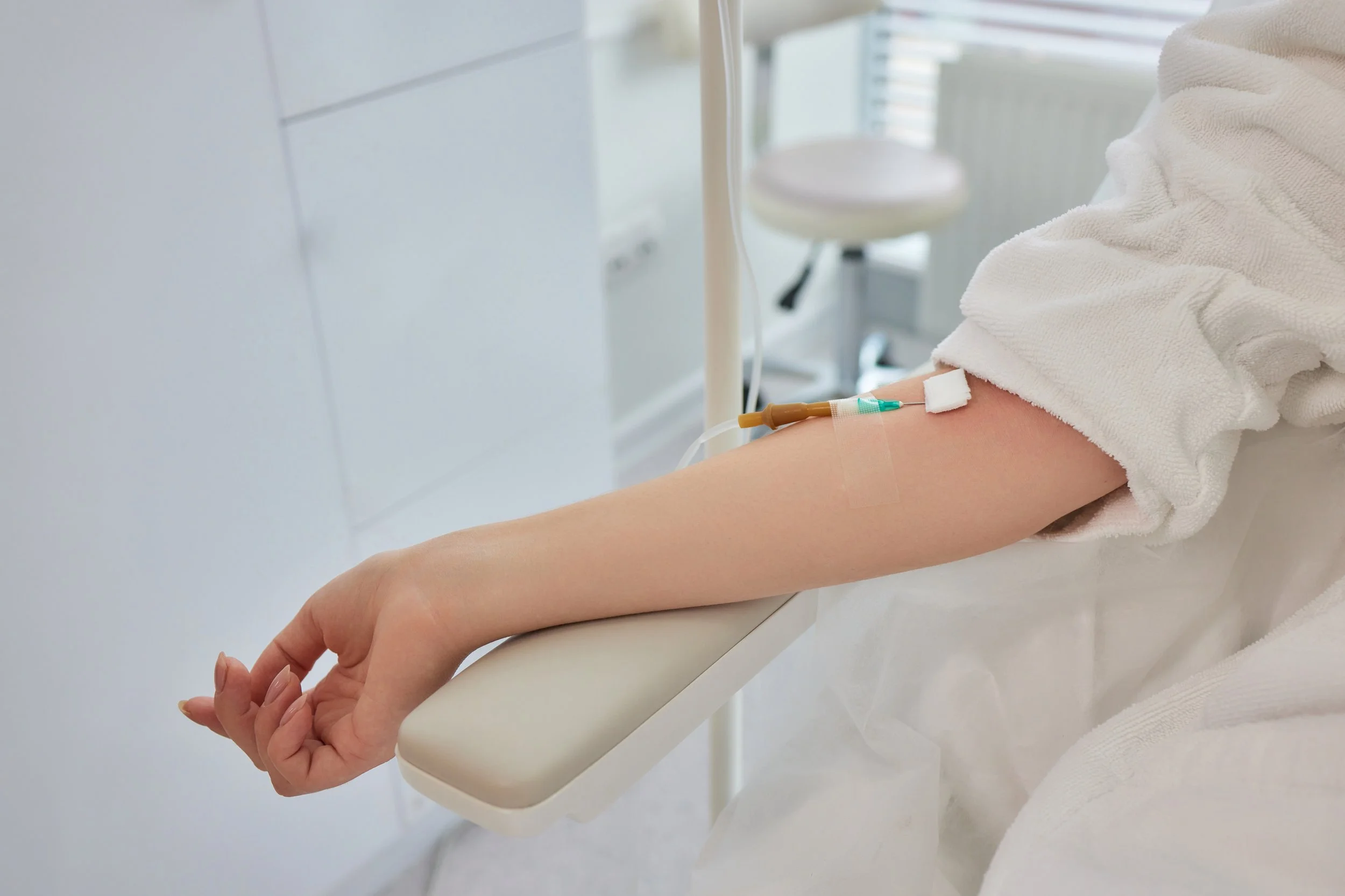 A person's arm on an adjustable armrest, with an intravenous (IV) needle and tubing inserted into the arm in a medical setting.