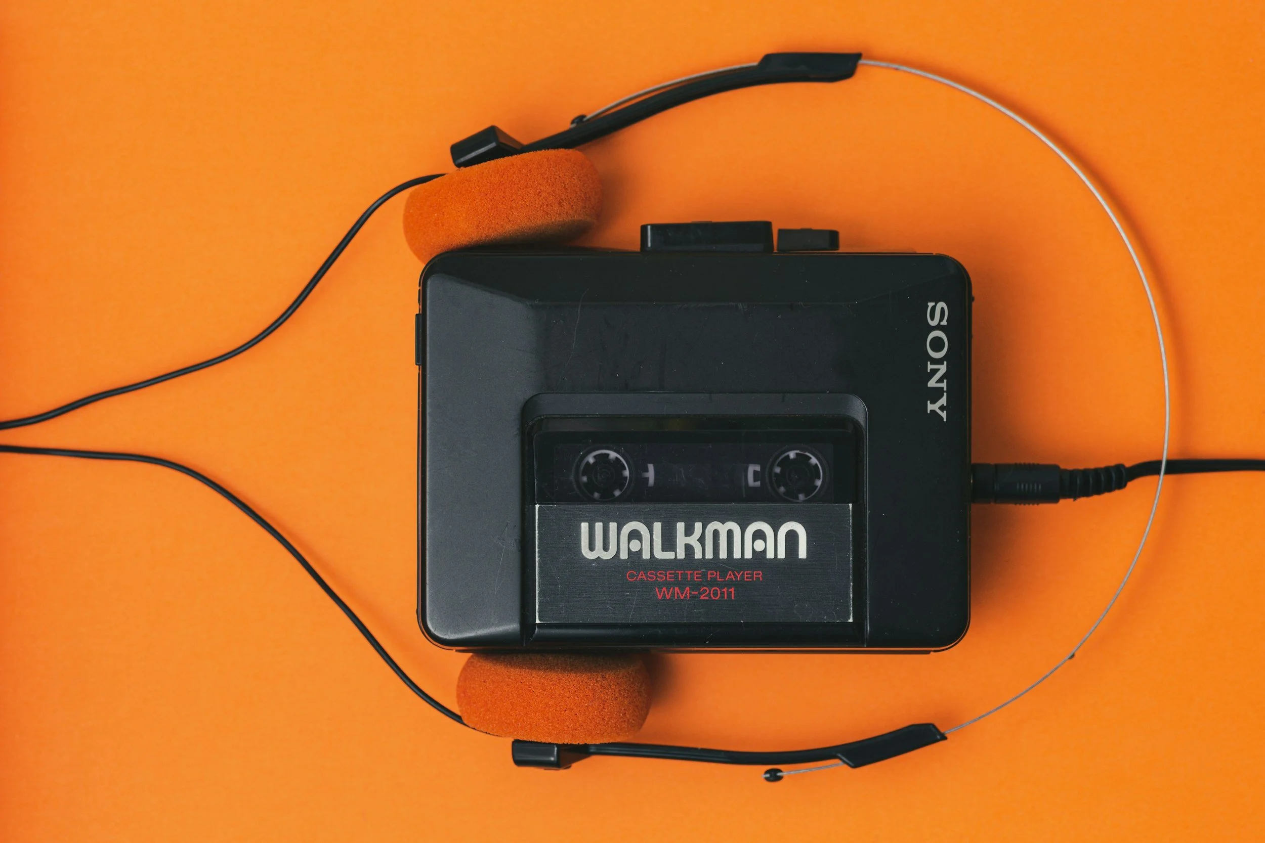 A vintage Sony Walkman cassette player with orange foam headphones on an orange surface.