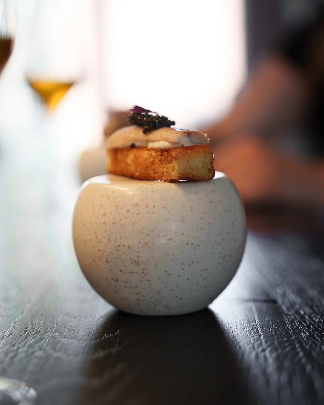 Gourmet canapé with caviar on bread placed on a spherical white dish.