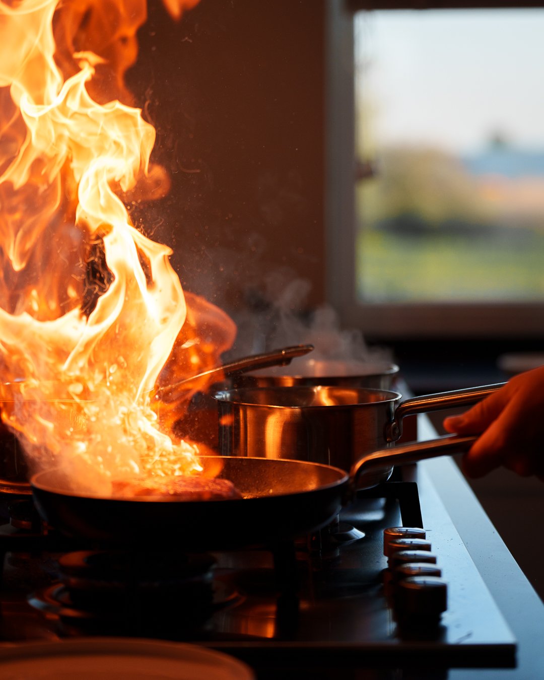Flames rising from a pan on a kitchen stove, with other pots in the background.