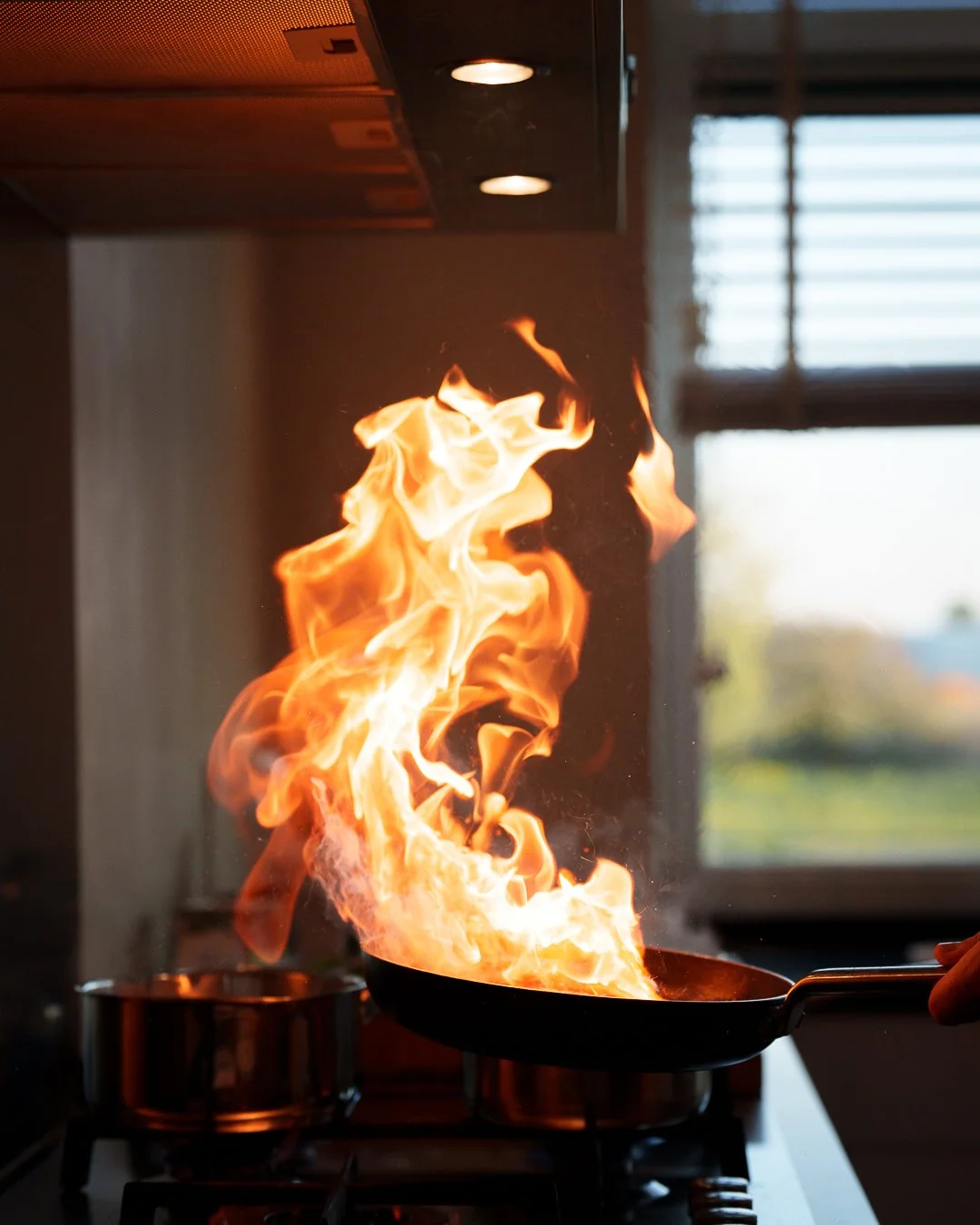 Flames rising from a frying pan on a stove in a kitchen.