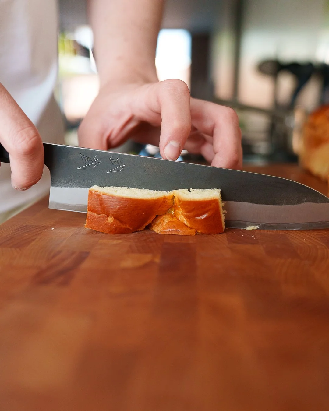 Person slicing bread on a wooden cutting board with a knife.