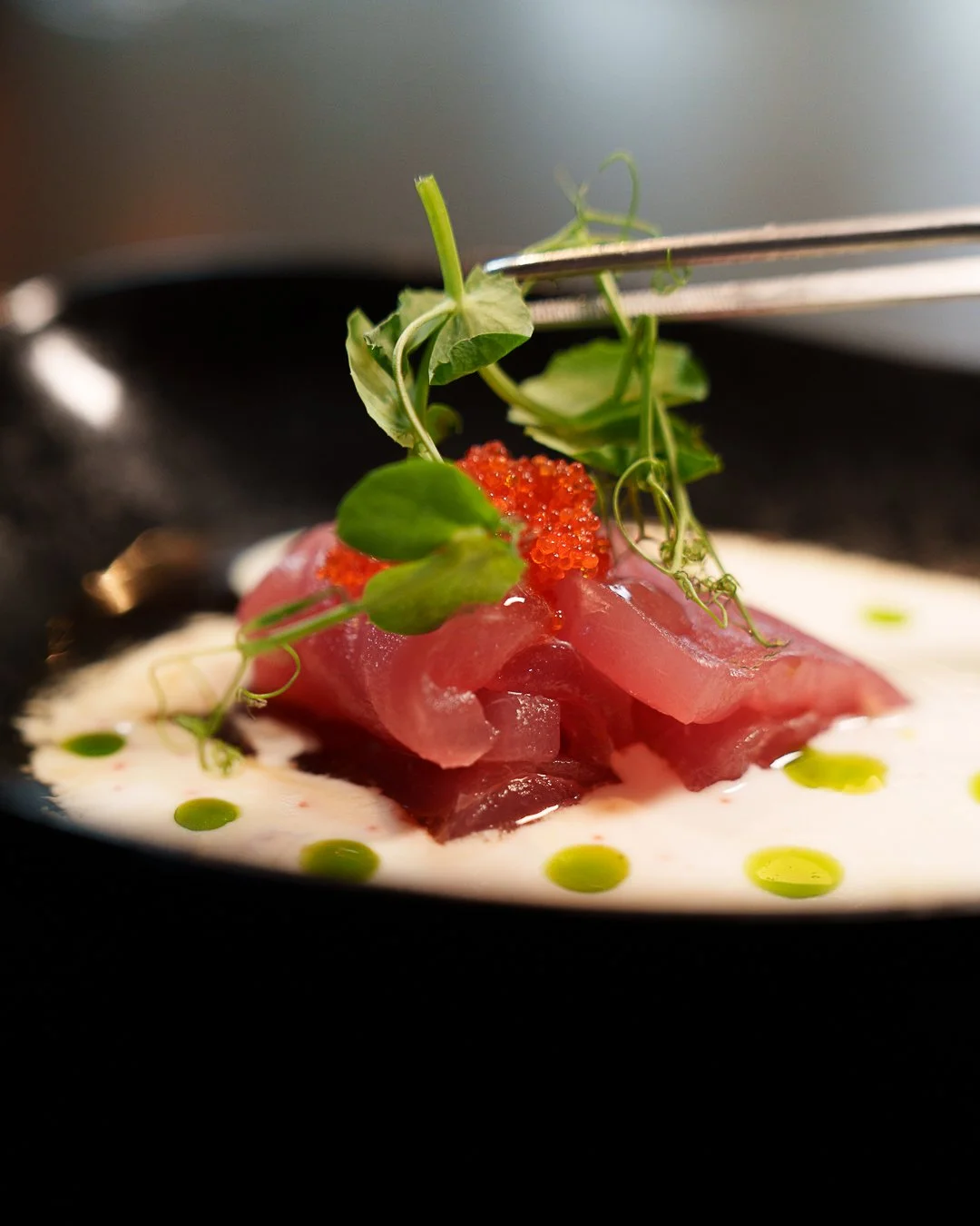 Gourmet dish with raw fish slices, microgreens, and roe on a creamy sauce, garnished with green oil droplets.