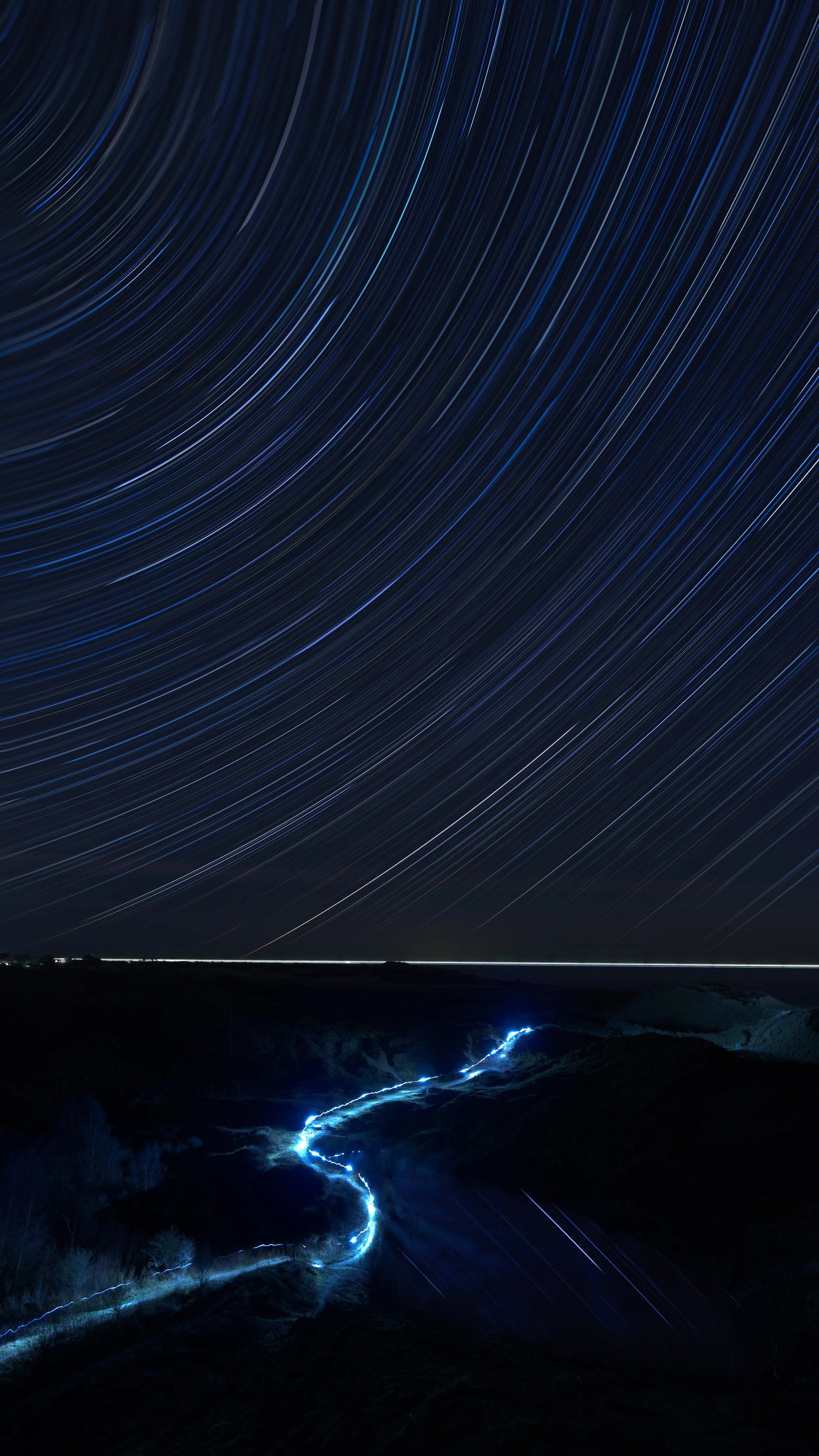 Buckroney Dunes, in Co Wicklow Ireland with star trails above and a glowing blue light trailing through the scenery