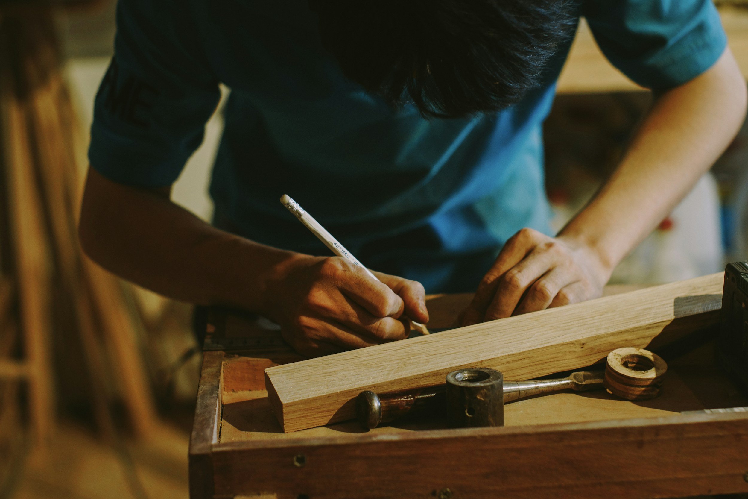 Person working on a woodworking project, using a pencil to mark a piece of wood, surrounded by tools and wood pieces.