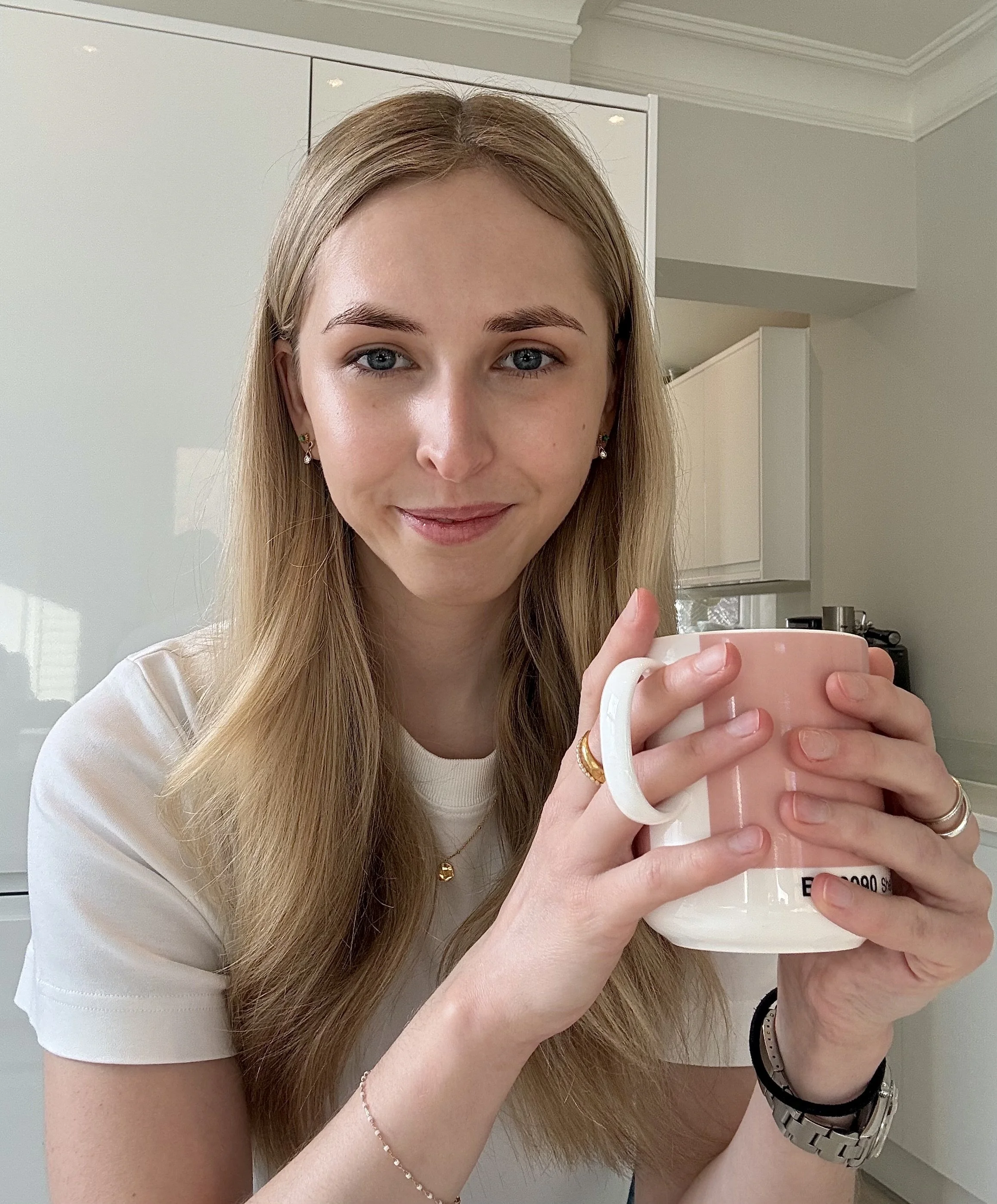 A young woman with blonde hair holding a pink mug in a kitchen.