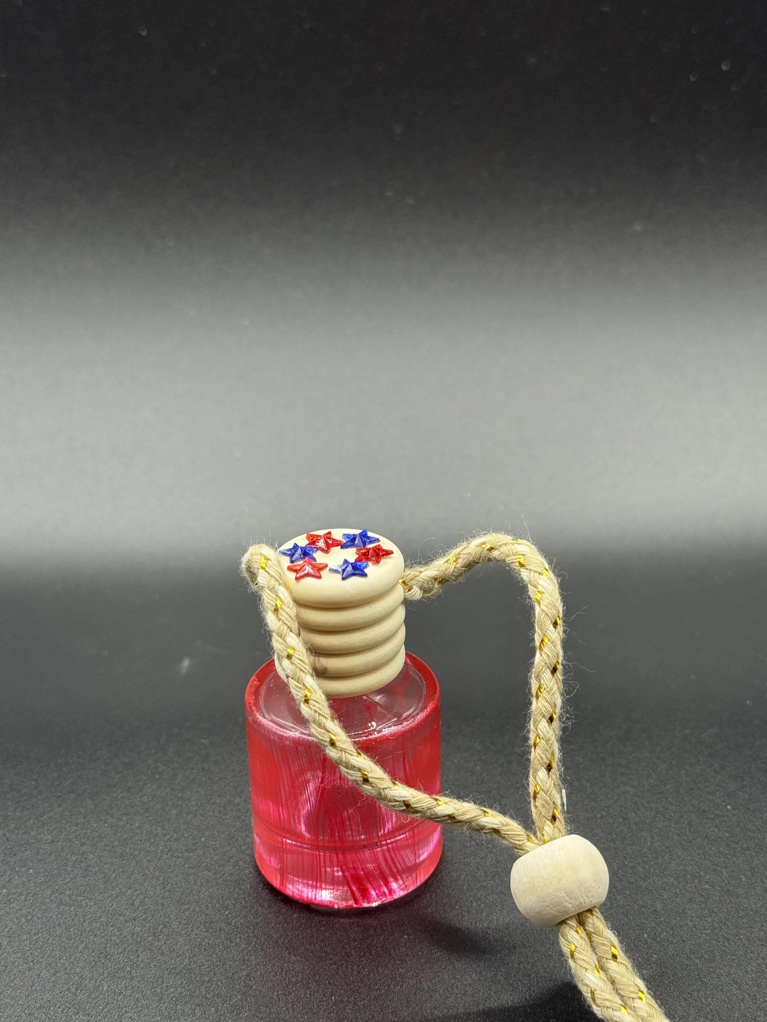 Small pink glass bottle with a wooden stopper, decorated with red and blue stars, and a braided yellow cord attached.