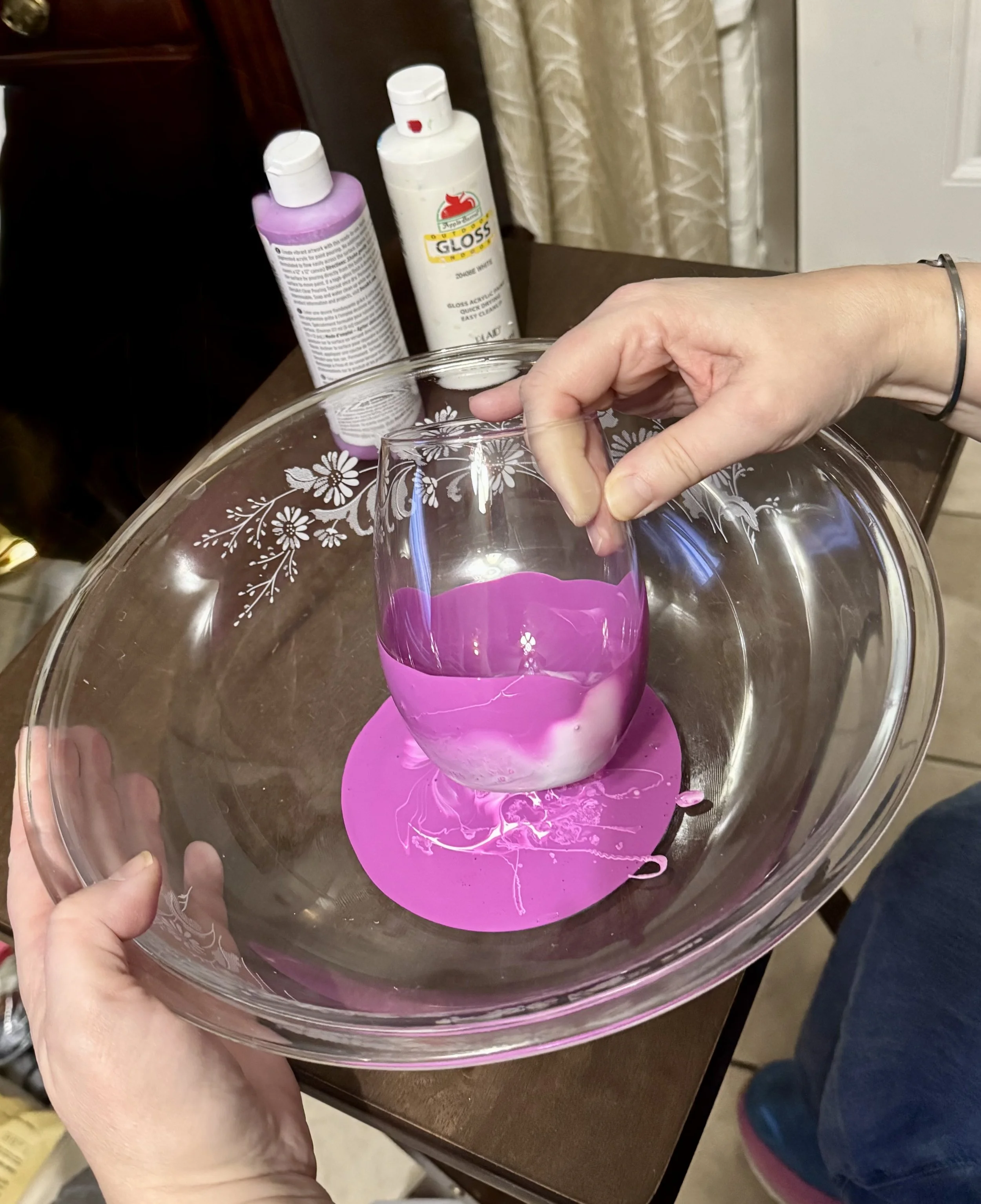 Amy using a clear glass bowl to dip a glass into paint
