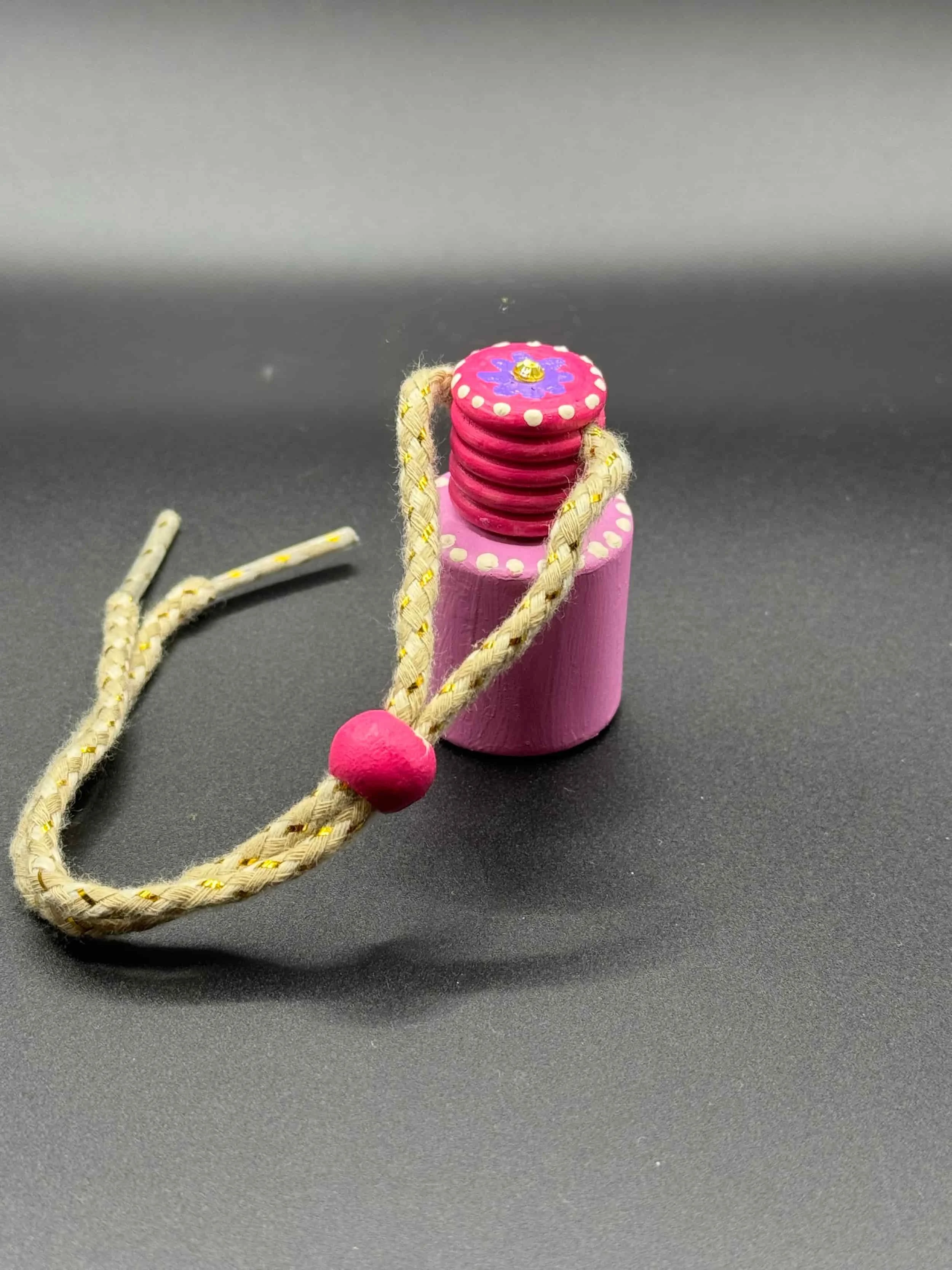 A small pink wooden top with a painted design and a braided string with a pink bead, set on a dark surface.