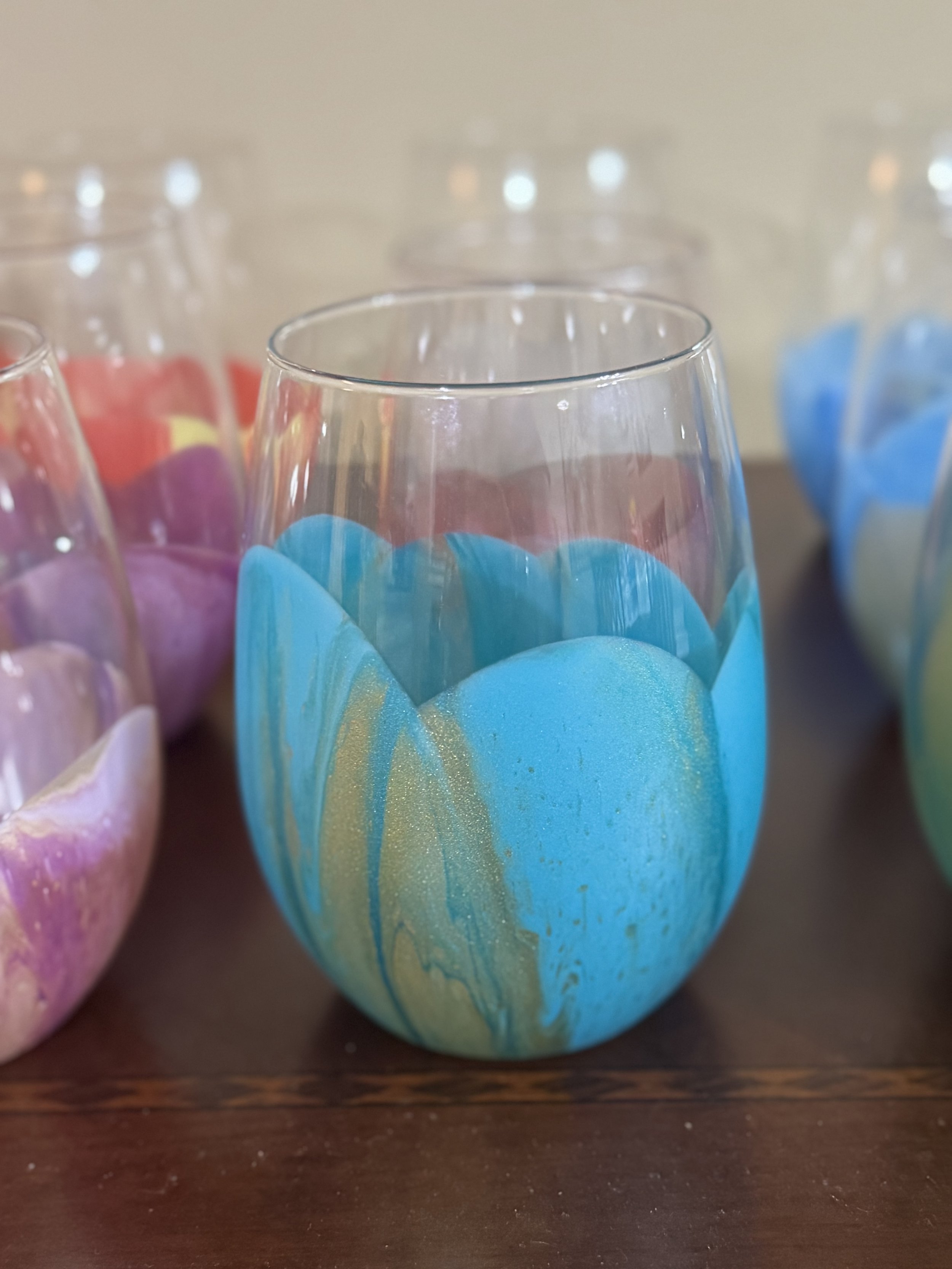 Close-up of colorfully painted glass cups on a wooden surface, featuring blue and gold swirls.
