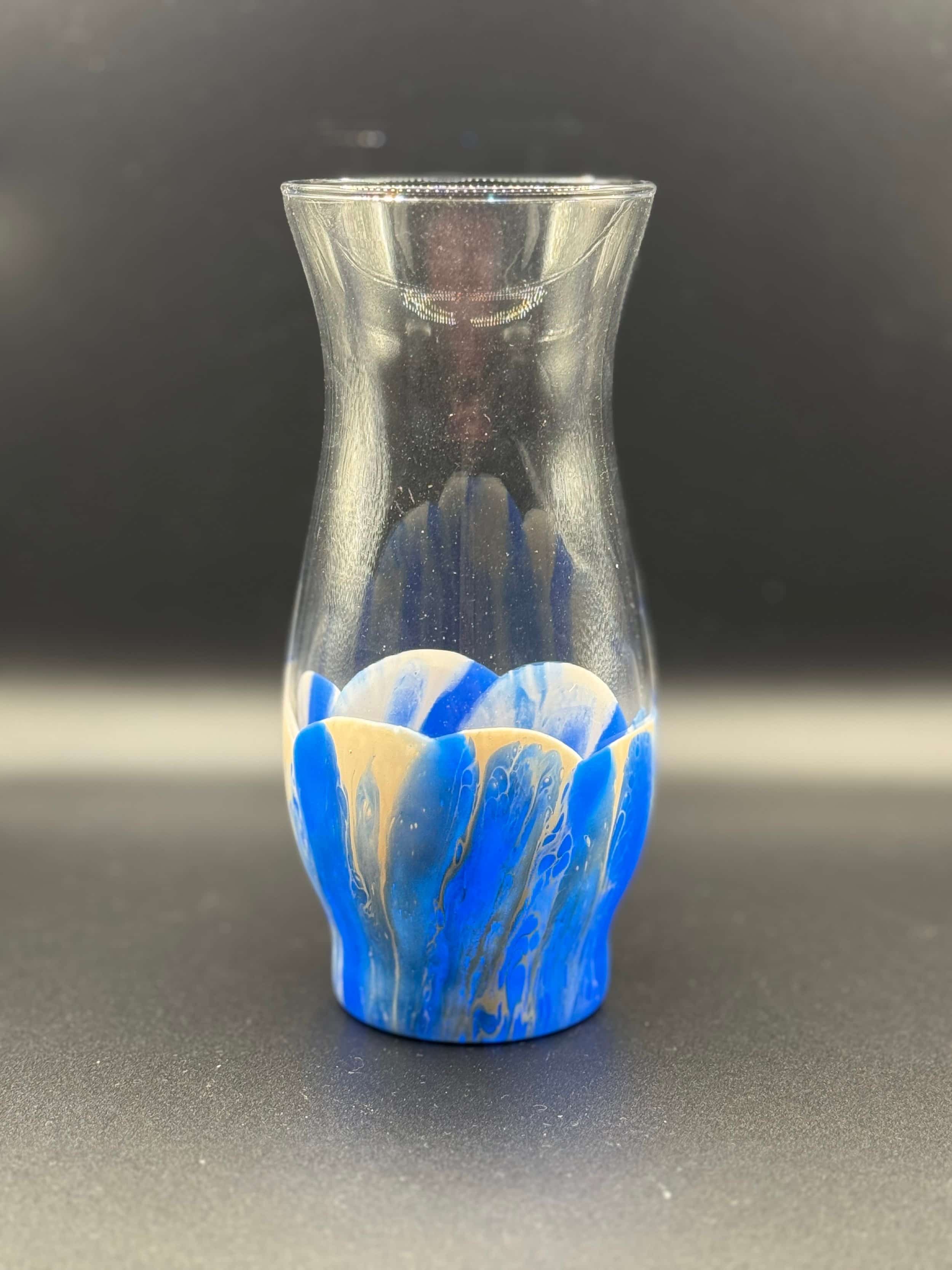 Clear glass vase with blue and beige abstract patterns at the base, set against a plain dark background.