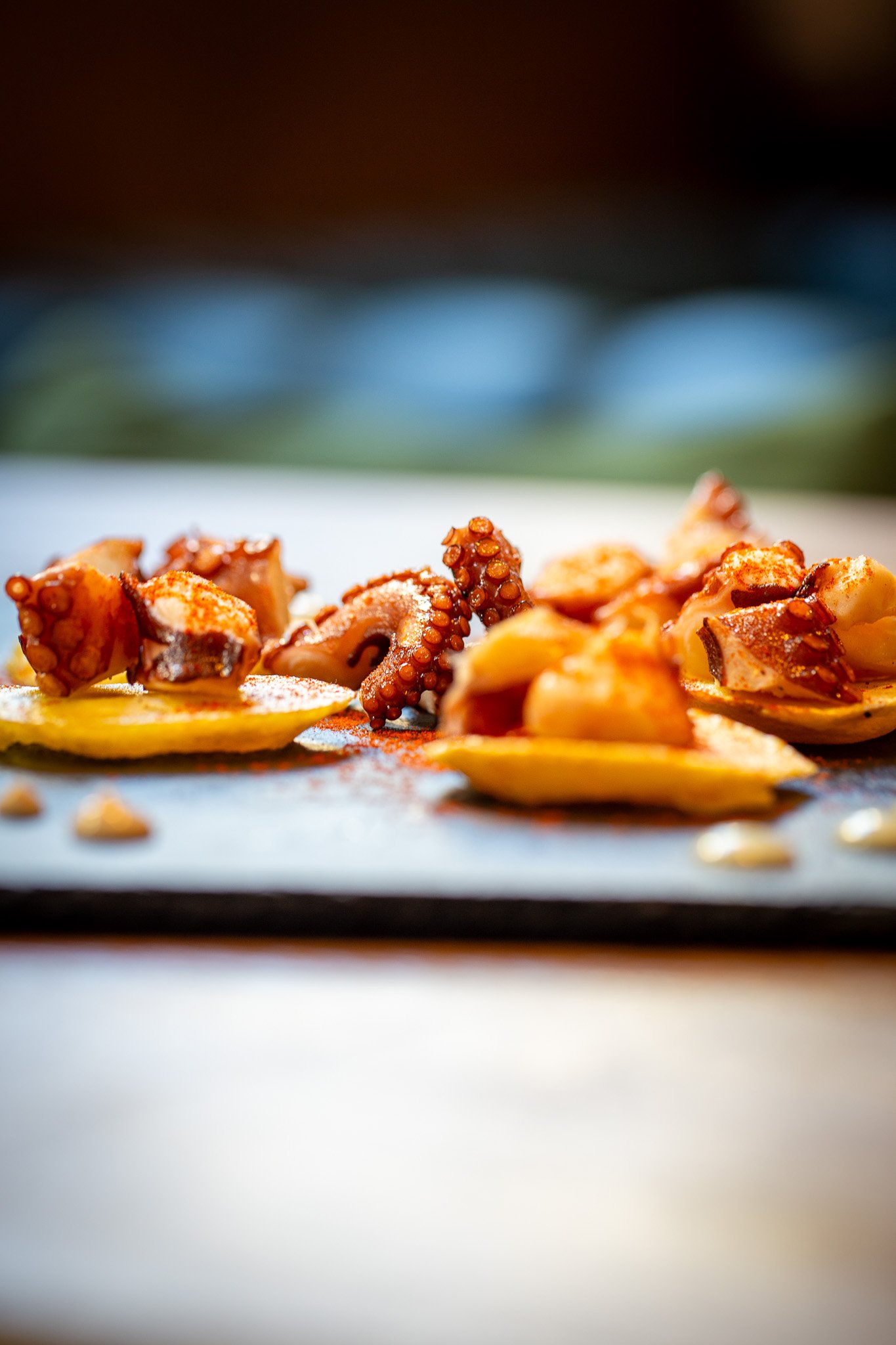 Tranches de poulpe grillé sur des rondelles de pomme de terre, saupoudrées de paprika, sur une assiette en ardoise.