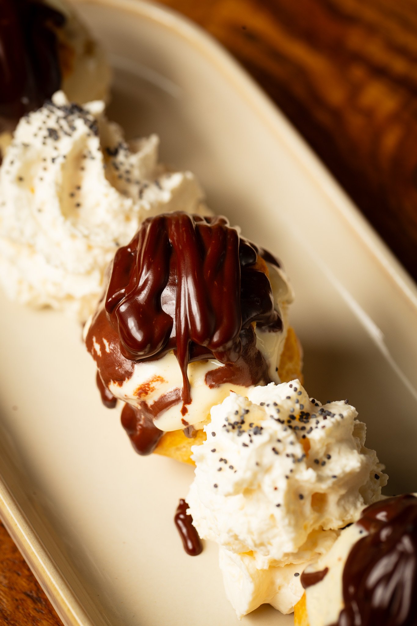 Chou à la crème garni de sauce au chocolat et de crème fouettée, présentés sur une assiette beige.
