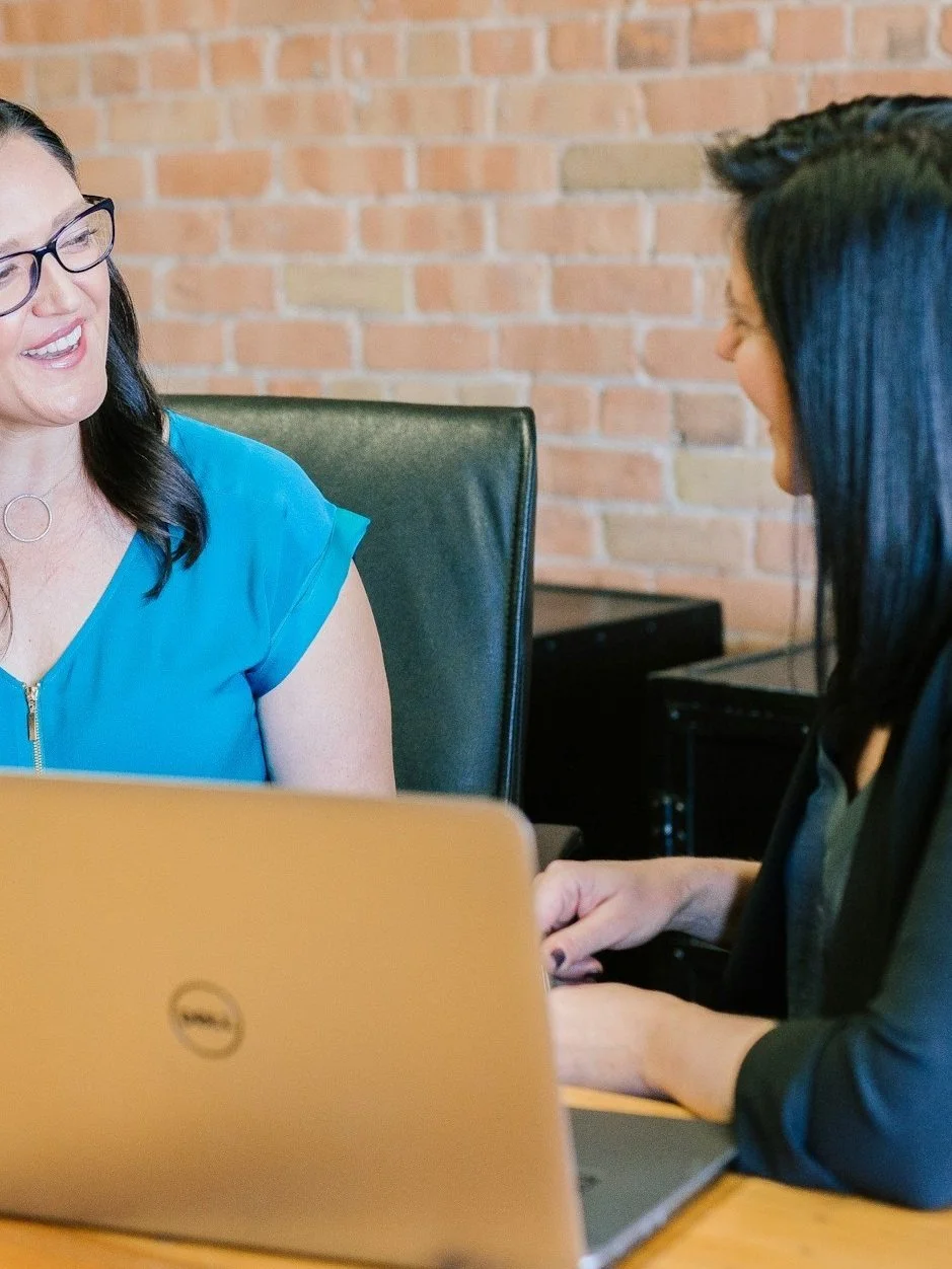 Two women having a meeting at a desk with a laptop.