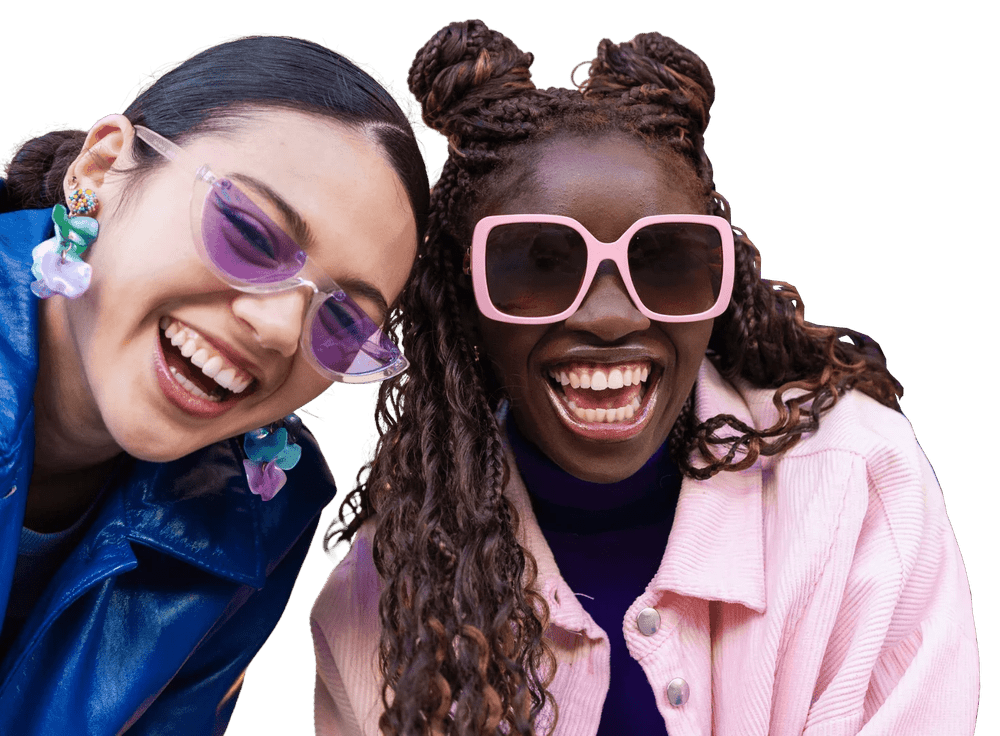 Two women laughing with colorful sunglasses, wearing trendy outfits, close-up portrait.