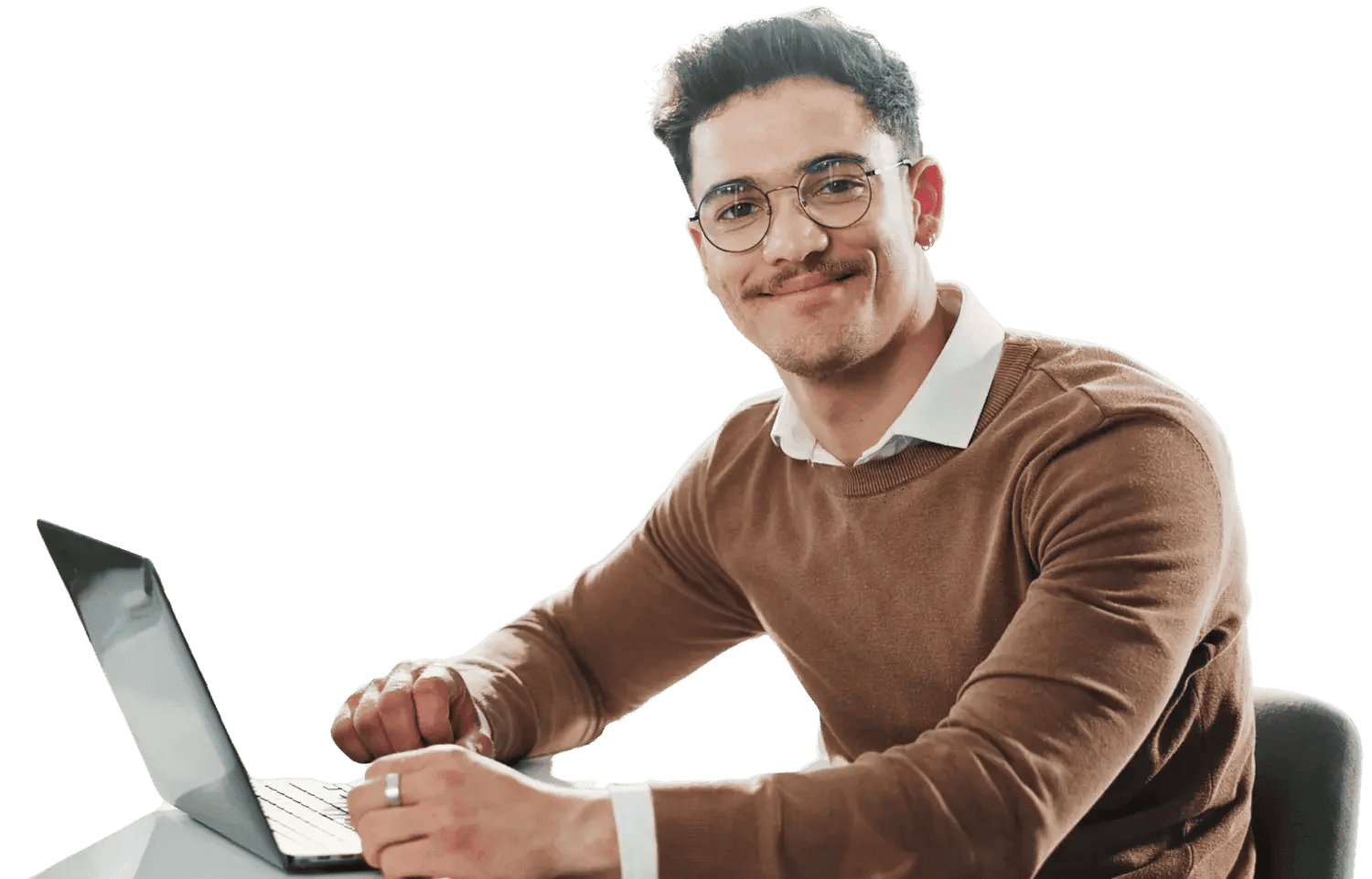 A man with glasses, a white shirt, and a brown sweater sitting at a desk with a laptop, smiling at the camera.