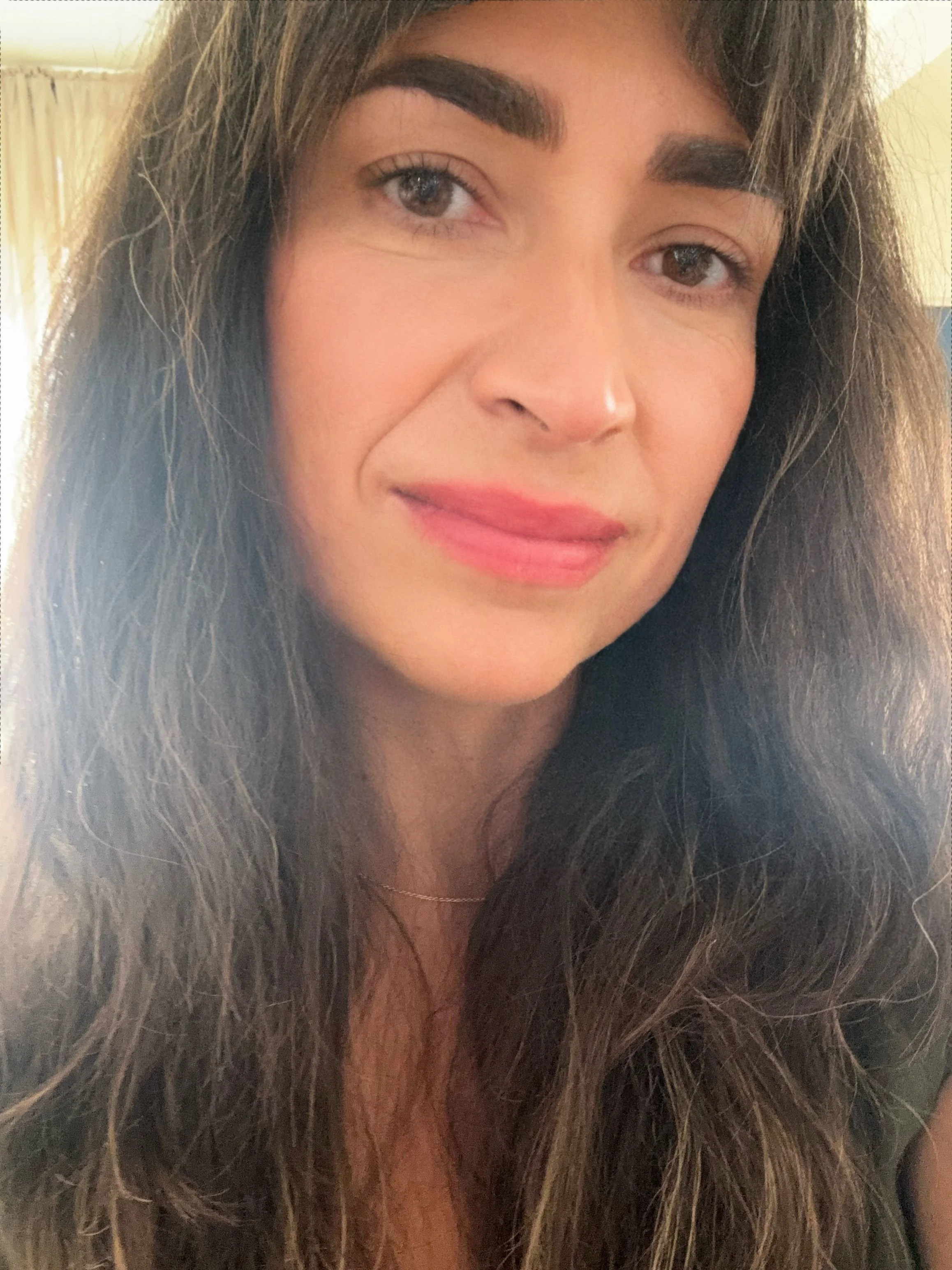 Close-up of a woman with long, curly brown hair, light brown eyes, and naturally pink lips, smiling softly.