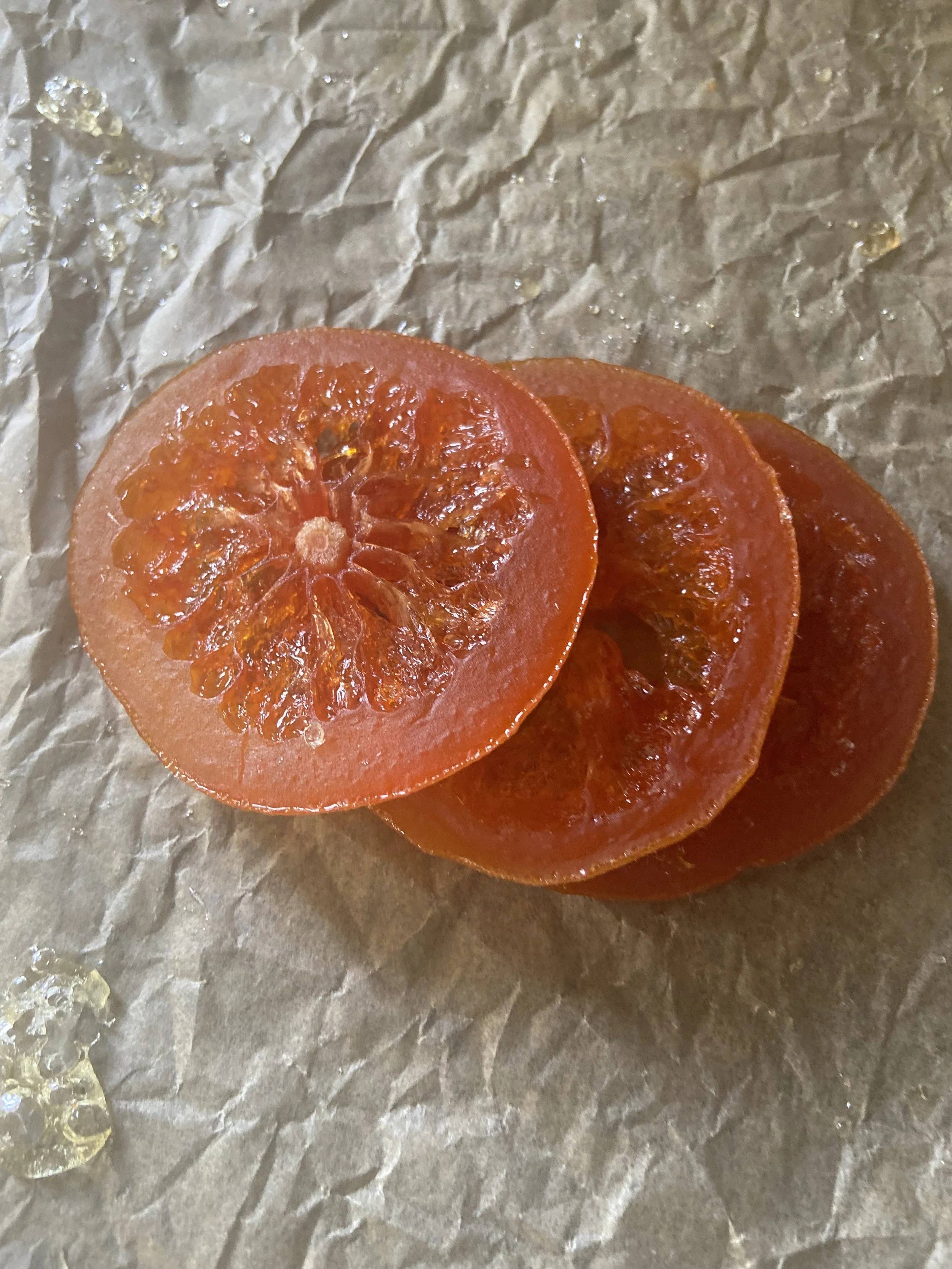 Slices of a candied blood orange on brown parchment paper.