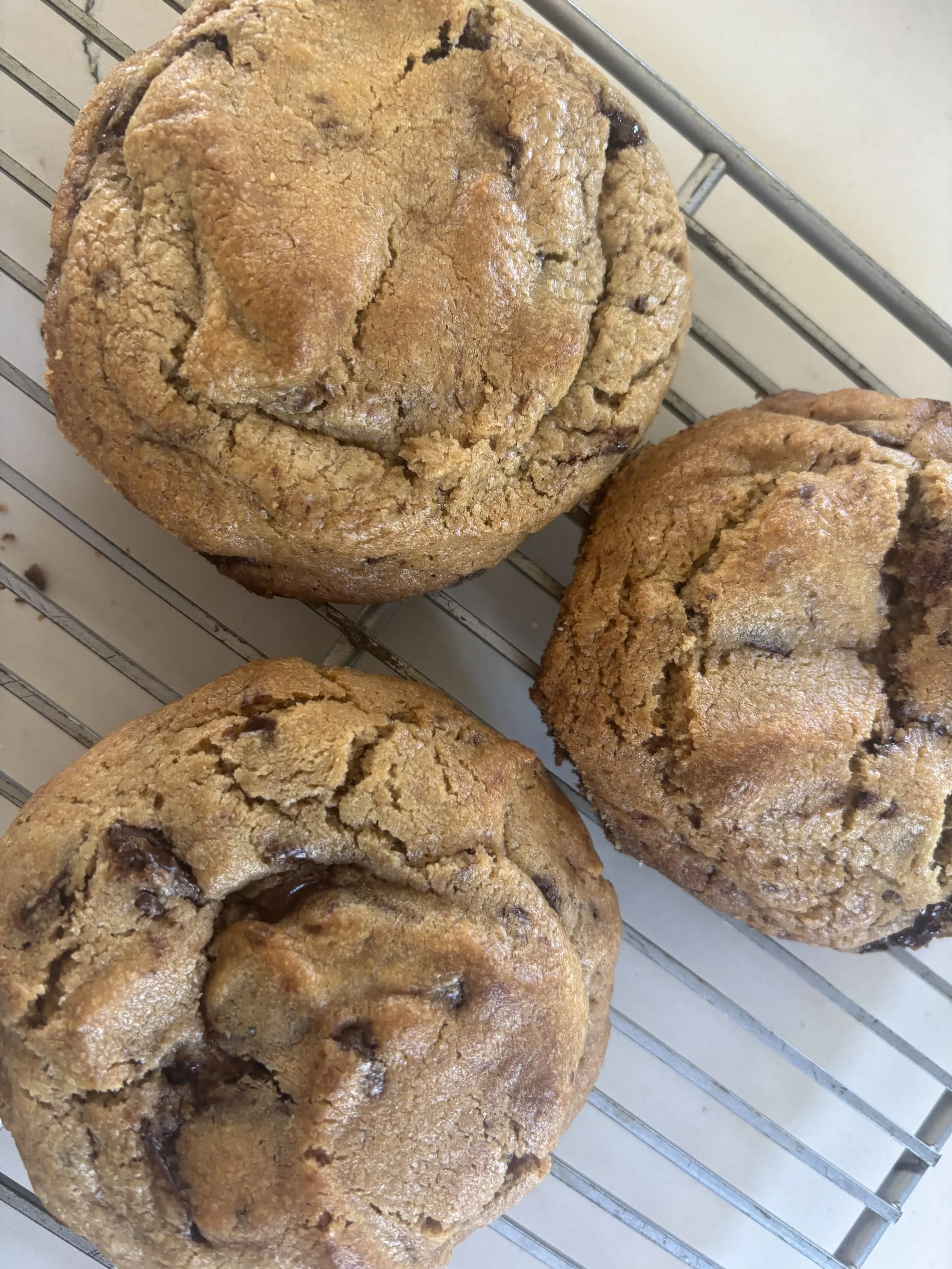 Three chocolate chip cookies on a wire cooling rack.