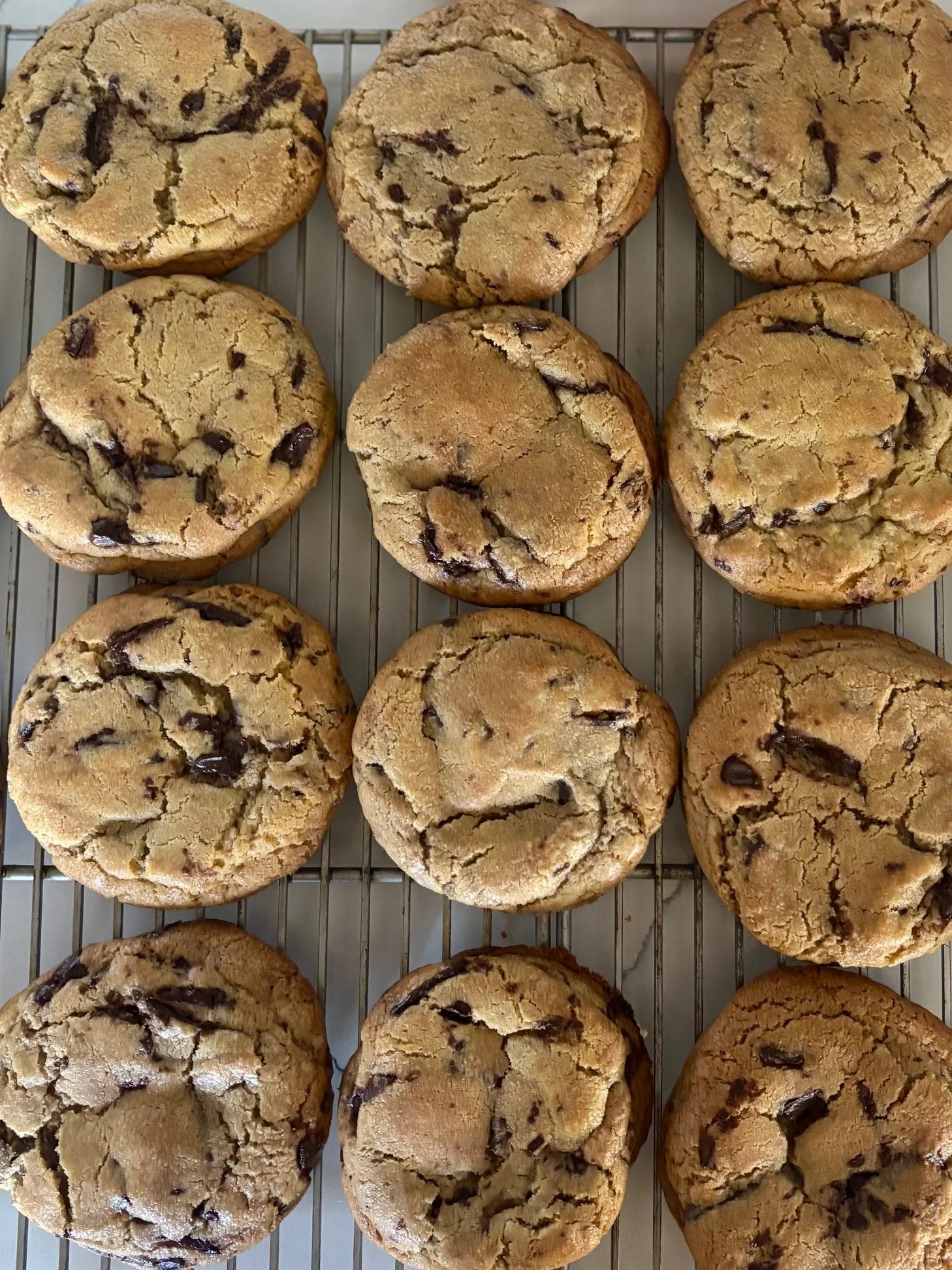 A cooling rack filled with freshly baked chocolate chip cookies.