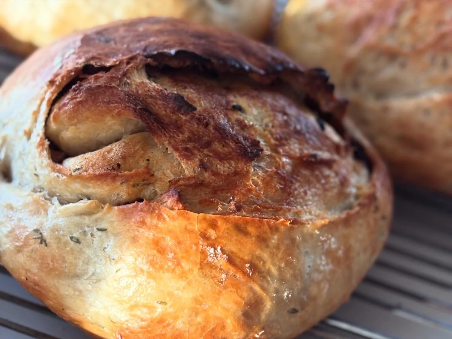 Close-up of a freshly baked bread roll with a crispy, golden-brown crust and a visible slit, resting on a wire rack.