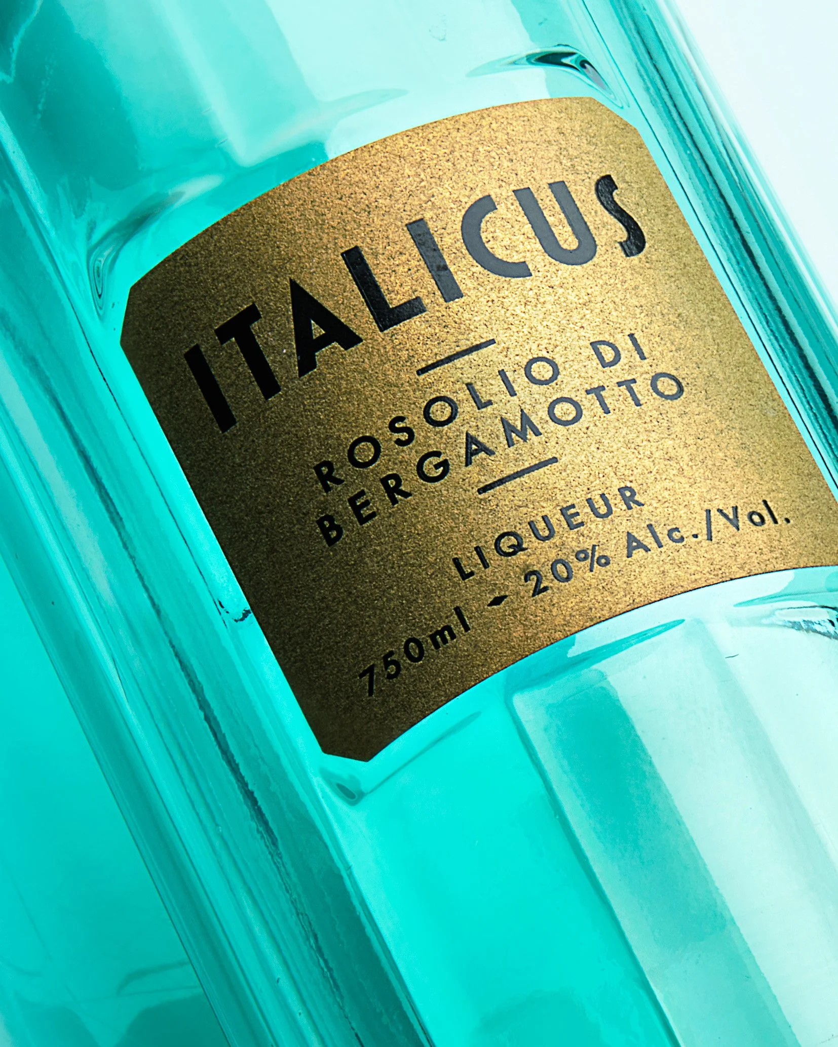 Close-up of a bottle of Italicus Rosolio di Bergamotto liqueur with a gold label and teal glass.