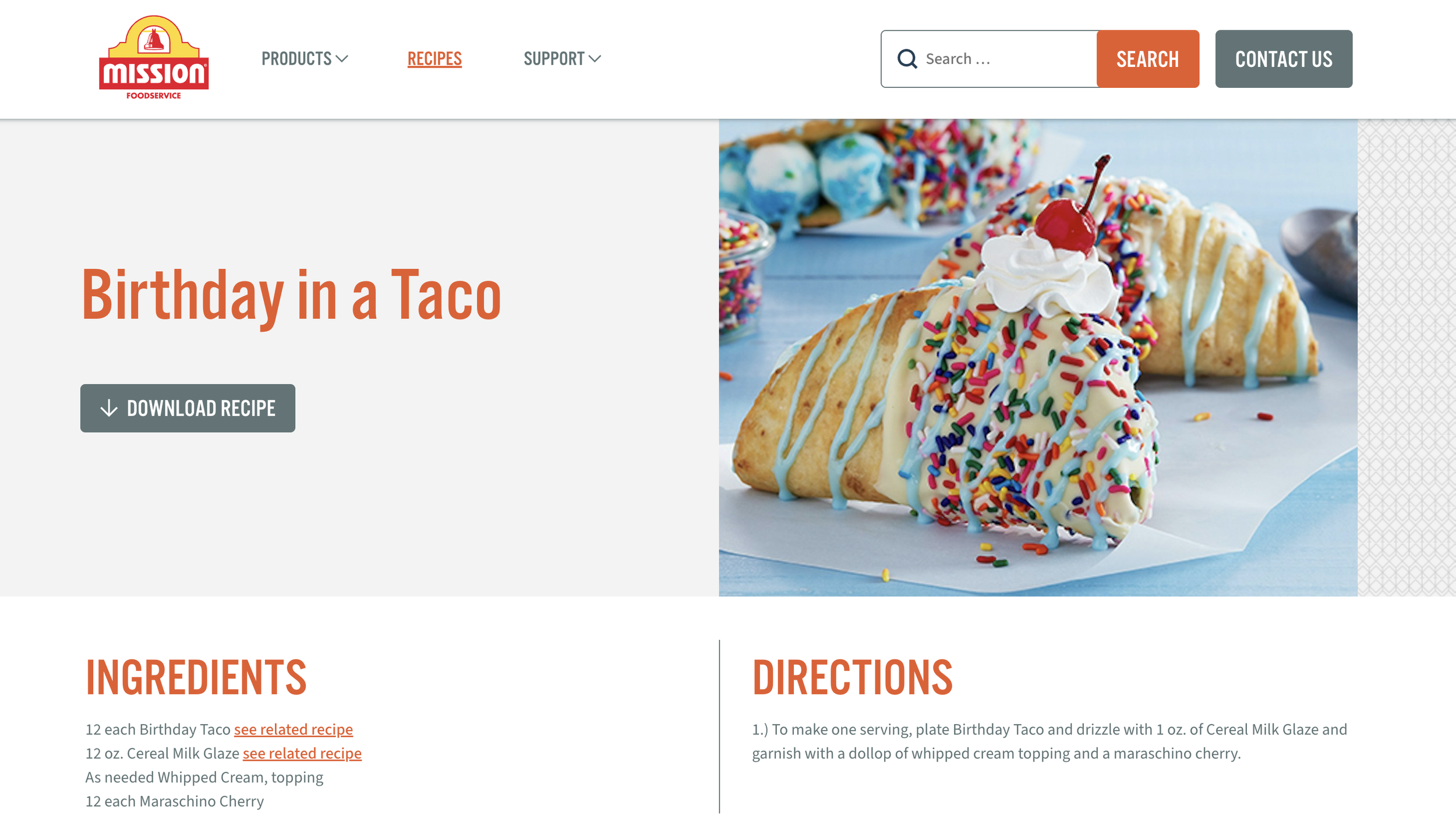 A surfboard-shaped birthday cake covered in white icing, colorful sprinkles, whipped cream, and a cherry on top, with a background of cupcakes and sweet treats.