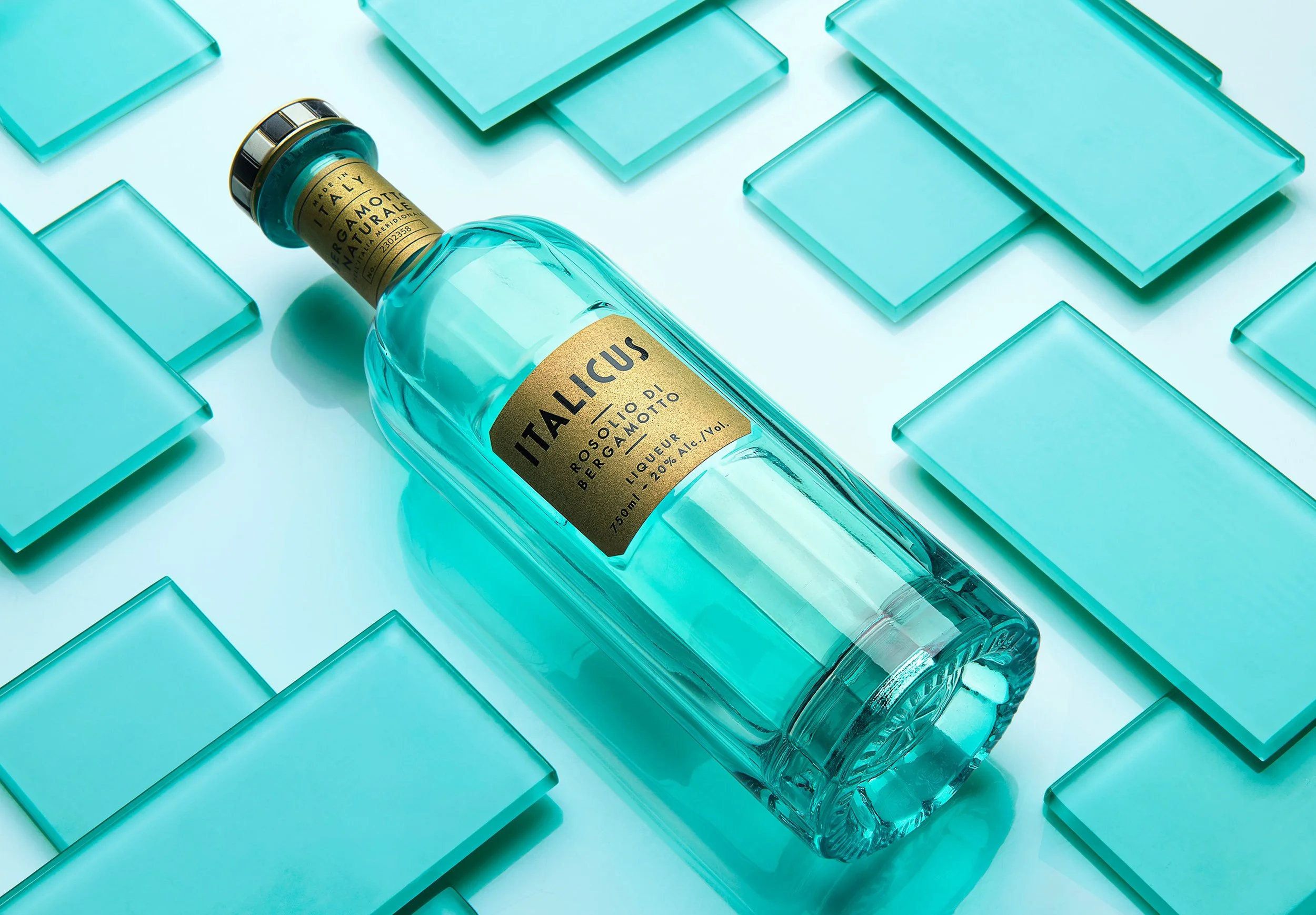 A glass bottle of Italicus Bergamot Liqueur lying on its side surrounded by turquoise square tiles.