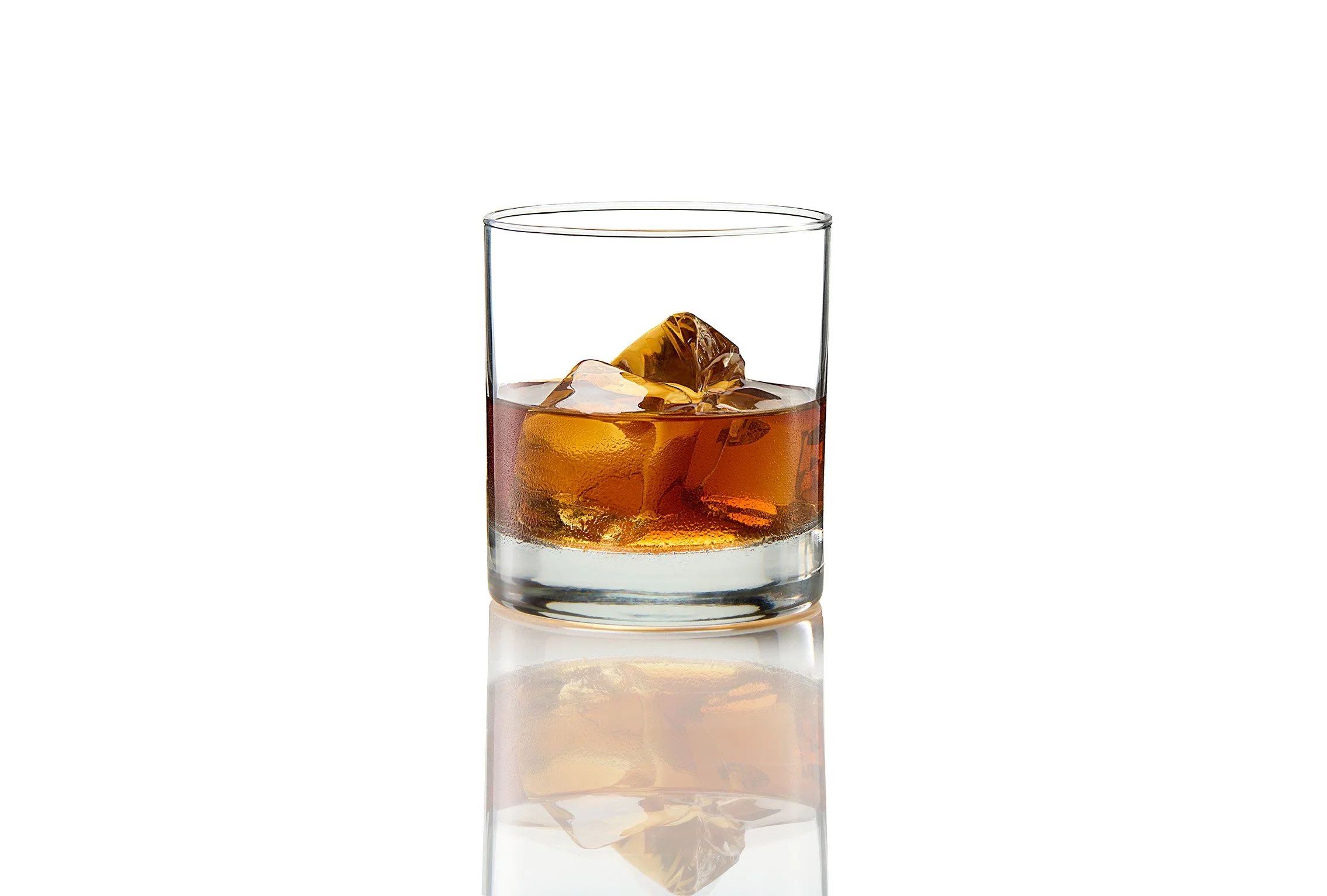 A glass of whiskey with ice cubes on a reflective surface with a white background.