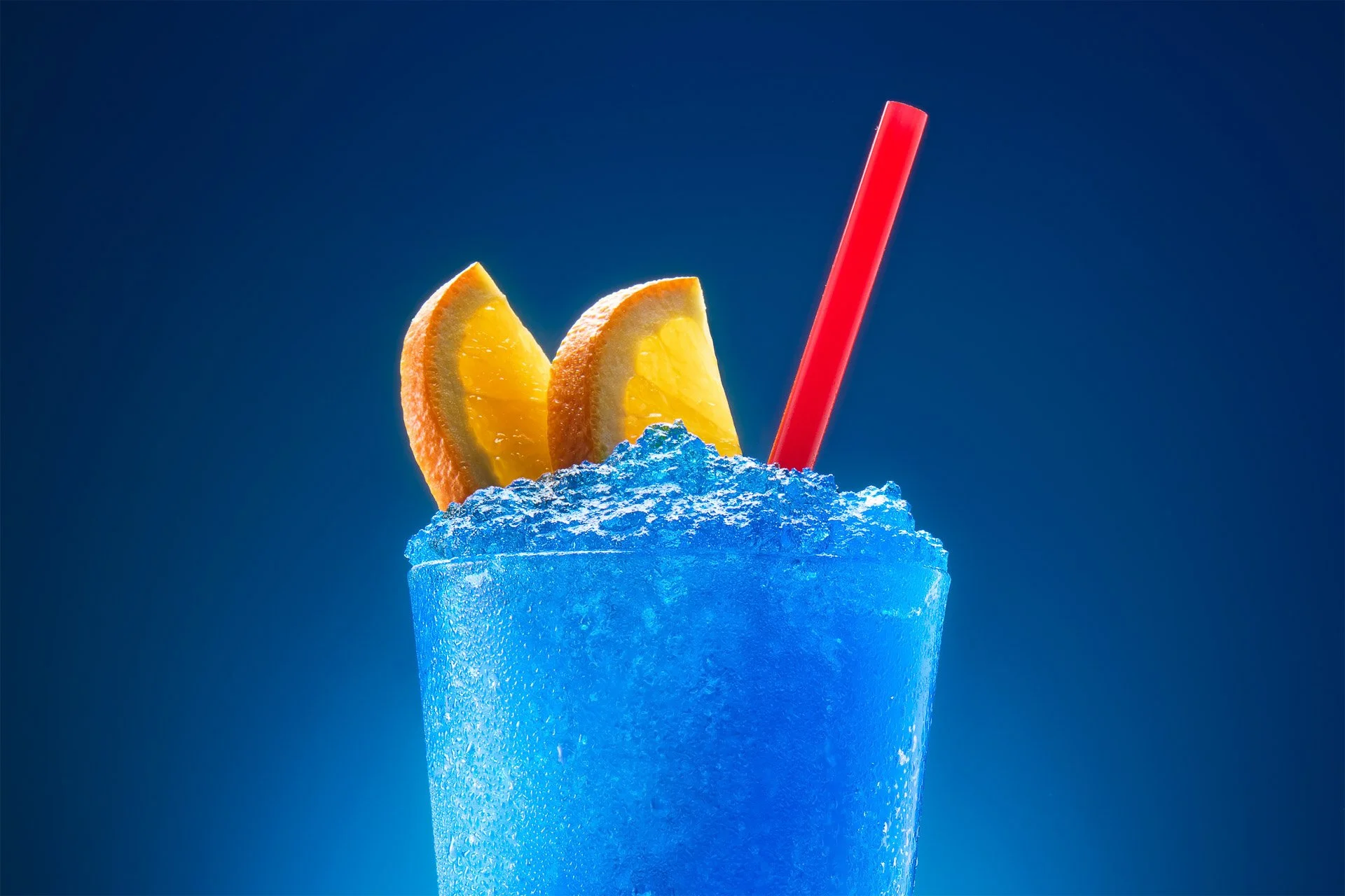 Blue frozen drink with lemon slices and a red straw garnished on top.