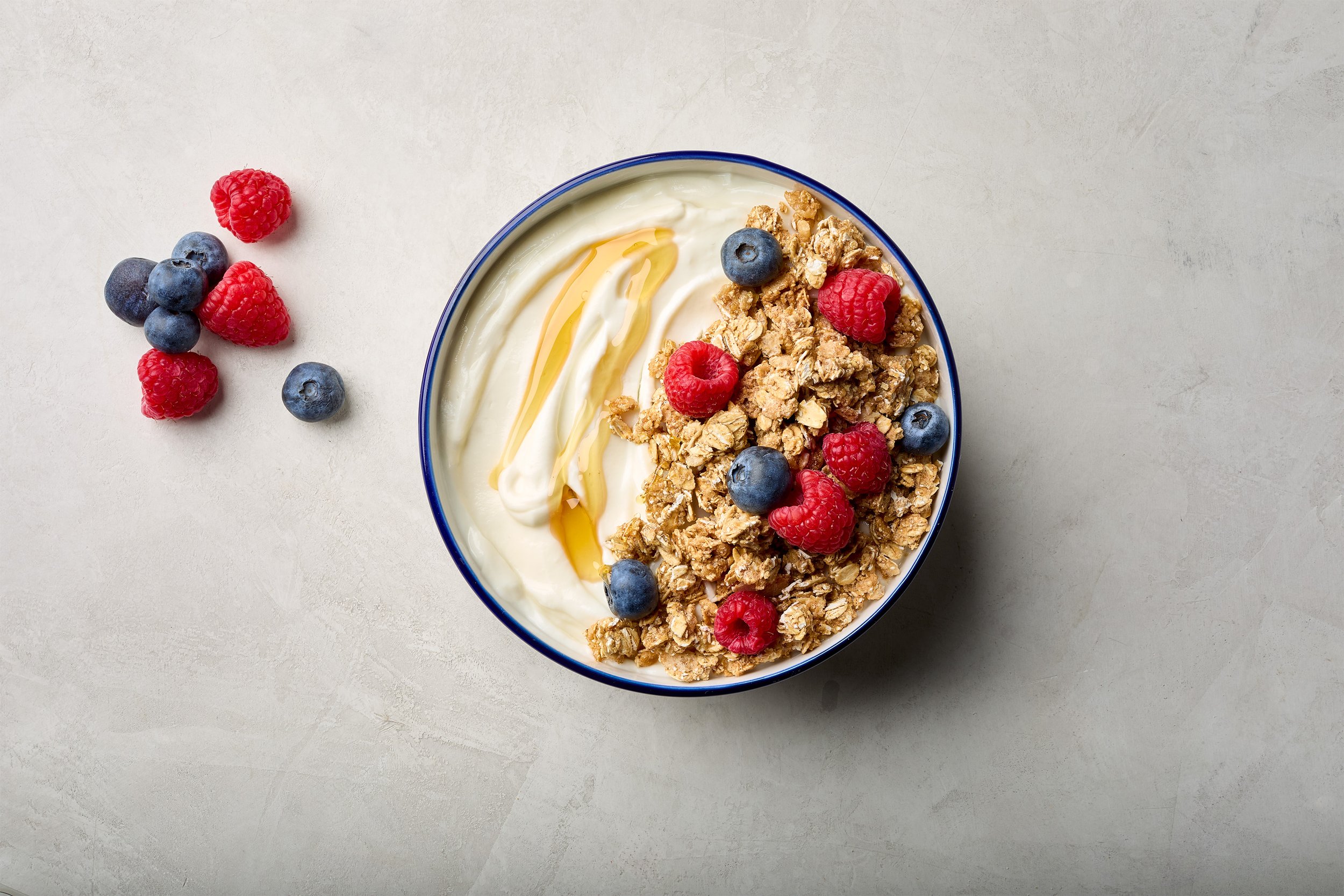 Bowl of yogurt topped with granola, raspberries, and blueberries, with additional berries on the side.