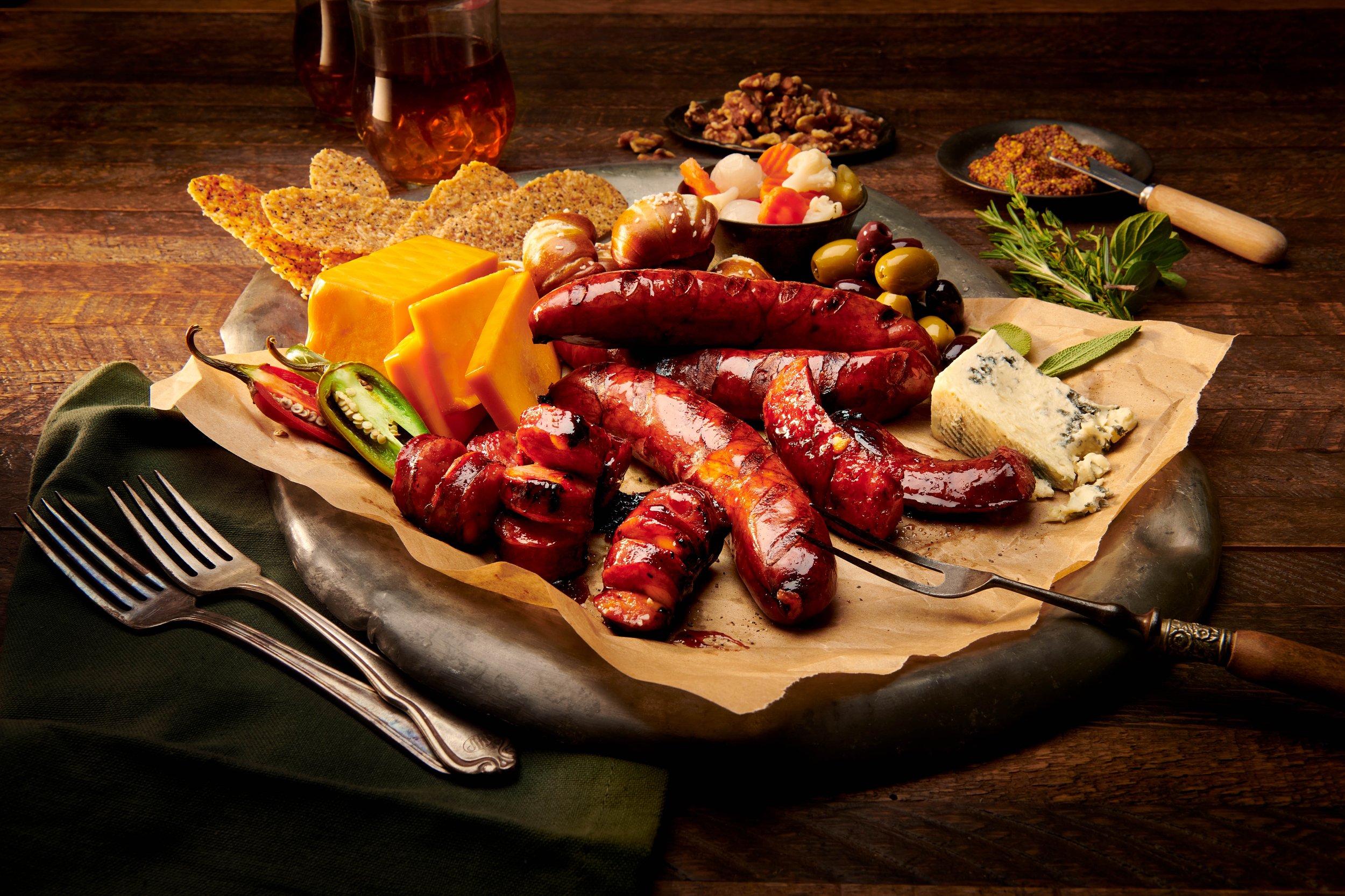 Charcuterie board with assorted cheeses, cured sausages, sliced peppers, pickles, nuts, and crackers, placed on a rustic wooden table with glasses of red wine.