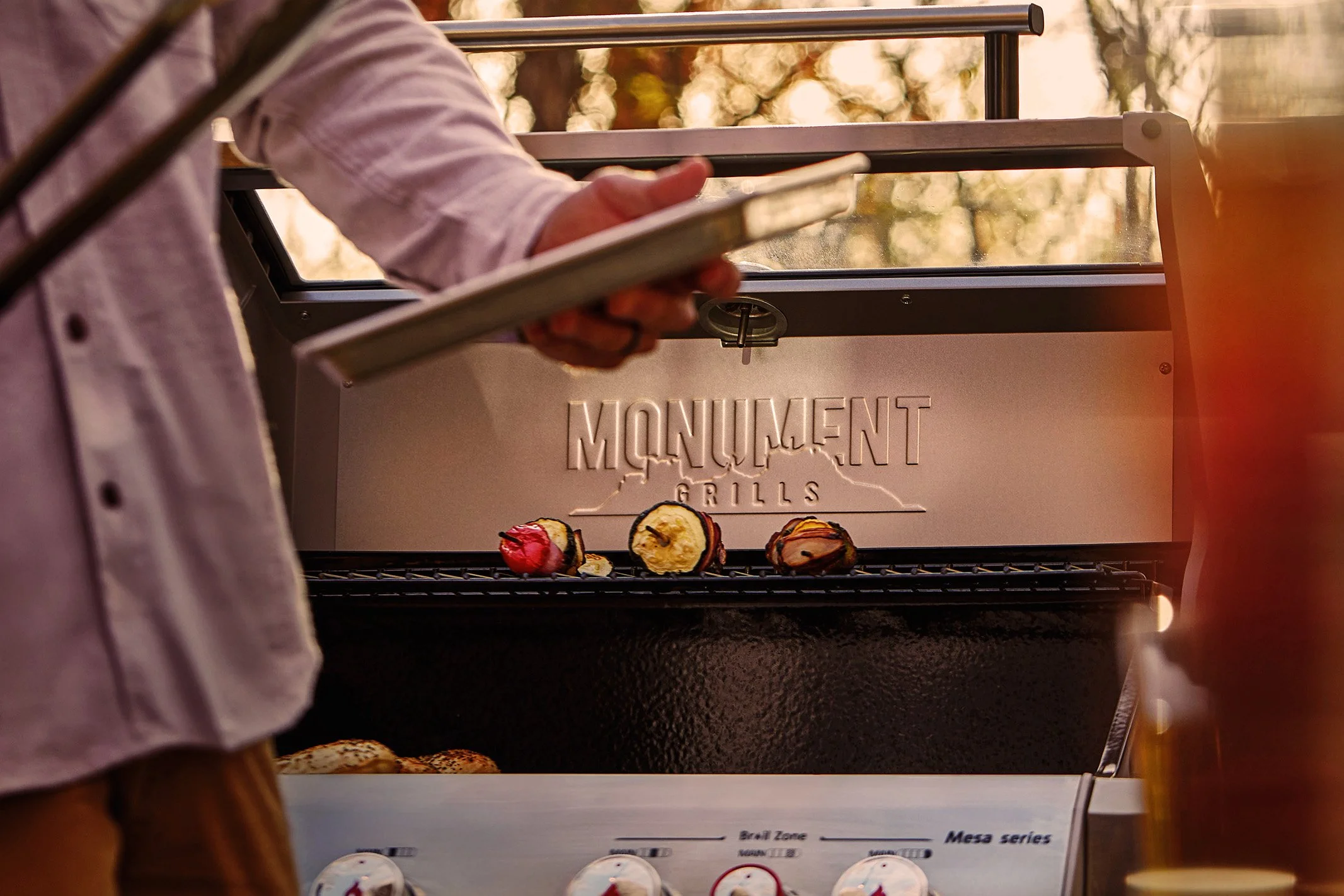 Person using a tablet to control a Monument Grills outdoor barbecue grill with grilled vegetables on it.