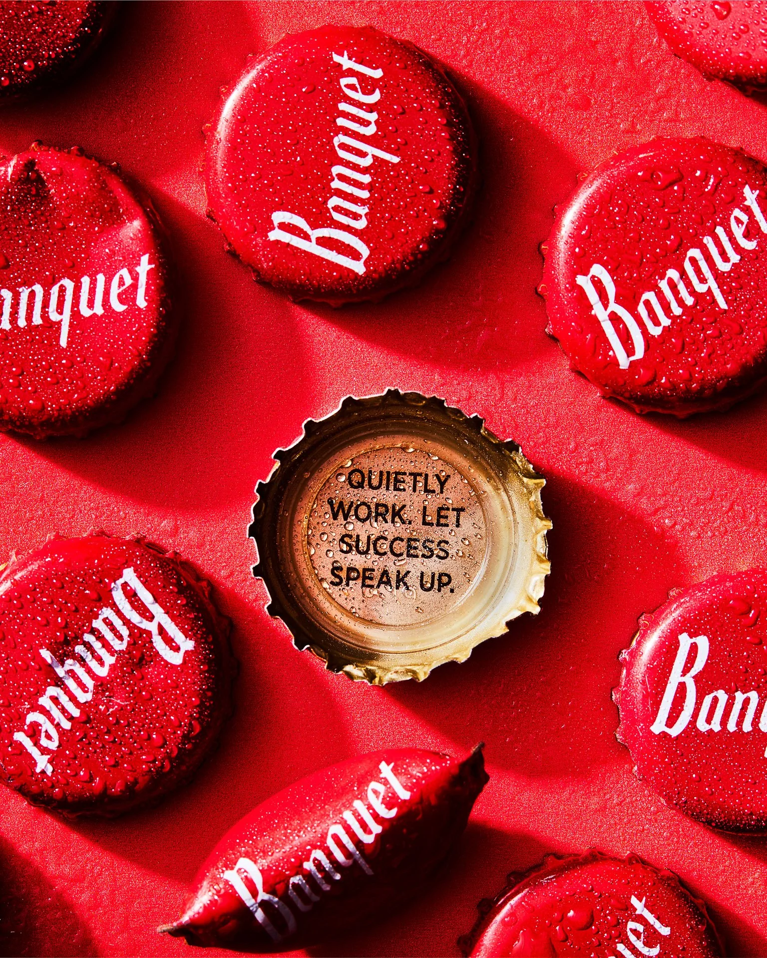 Red beer bottle caps with 'Banquet' text, and one open cap with the message 'Quietly work. Let success speak up.'