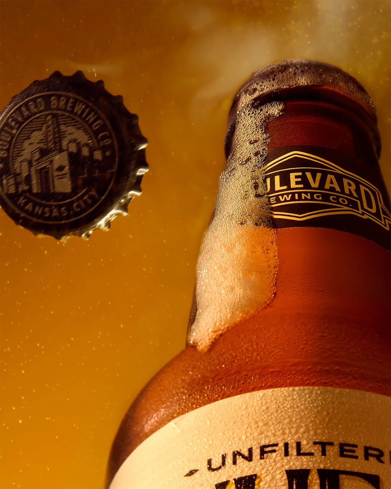 A close-up of a beer bottle with foam and condensation, with a label reading 'Unfiltered,' alongside a bottle cap showing 'Bled Brewing Co., Kansas City.'