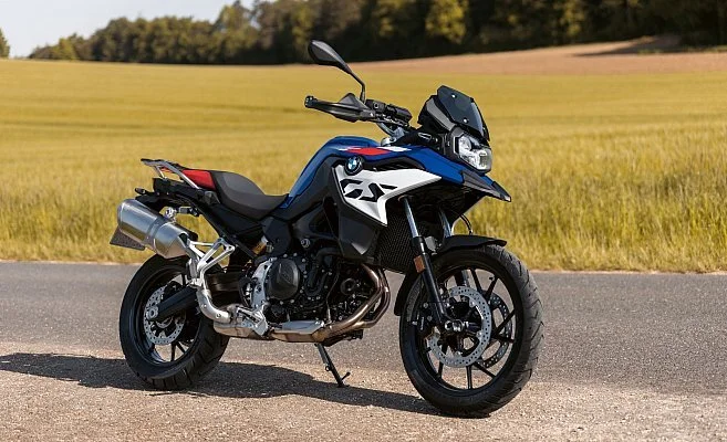 Blue and black BMW adventure motorcycle parked on the side of a rural road with a field and trees in the background.