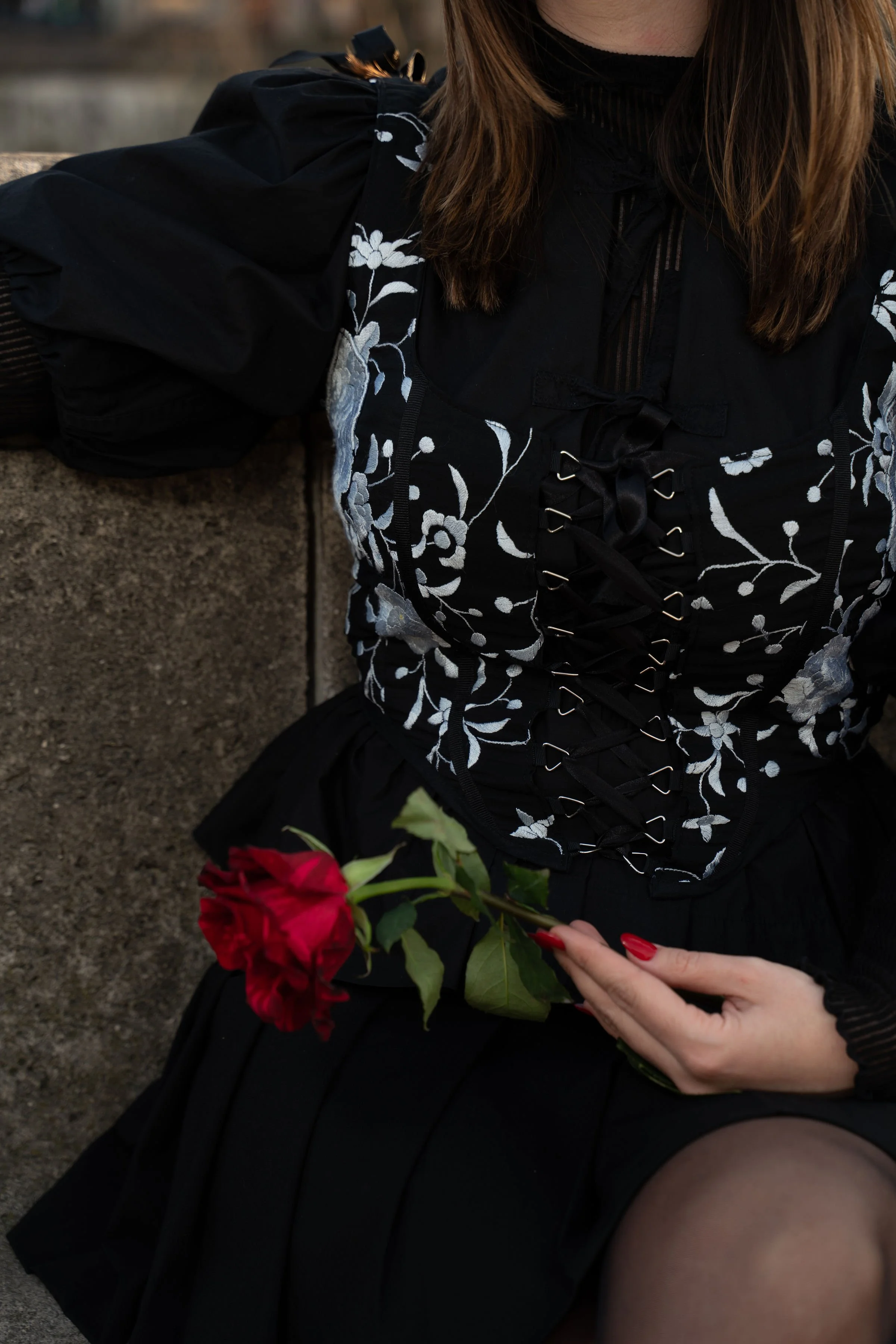 Mujer con ropa negra y bordados florales sostiene una rosa roja.