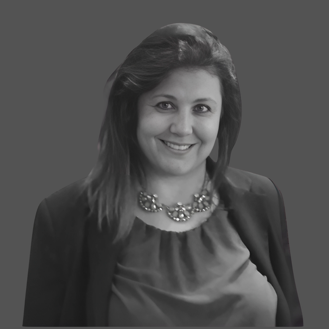 Black and white photo of a woman with shoulder-length hair, smiling, wearing a blouse, blazer, and a statement necklace.