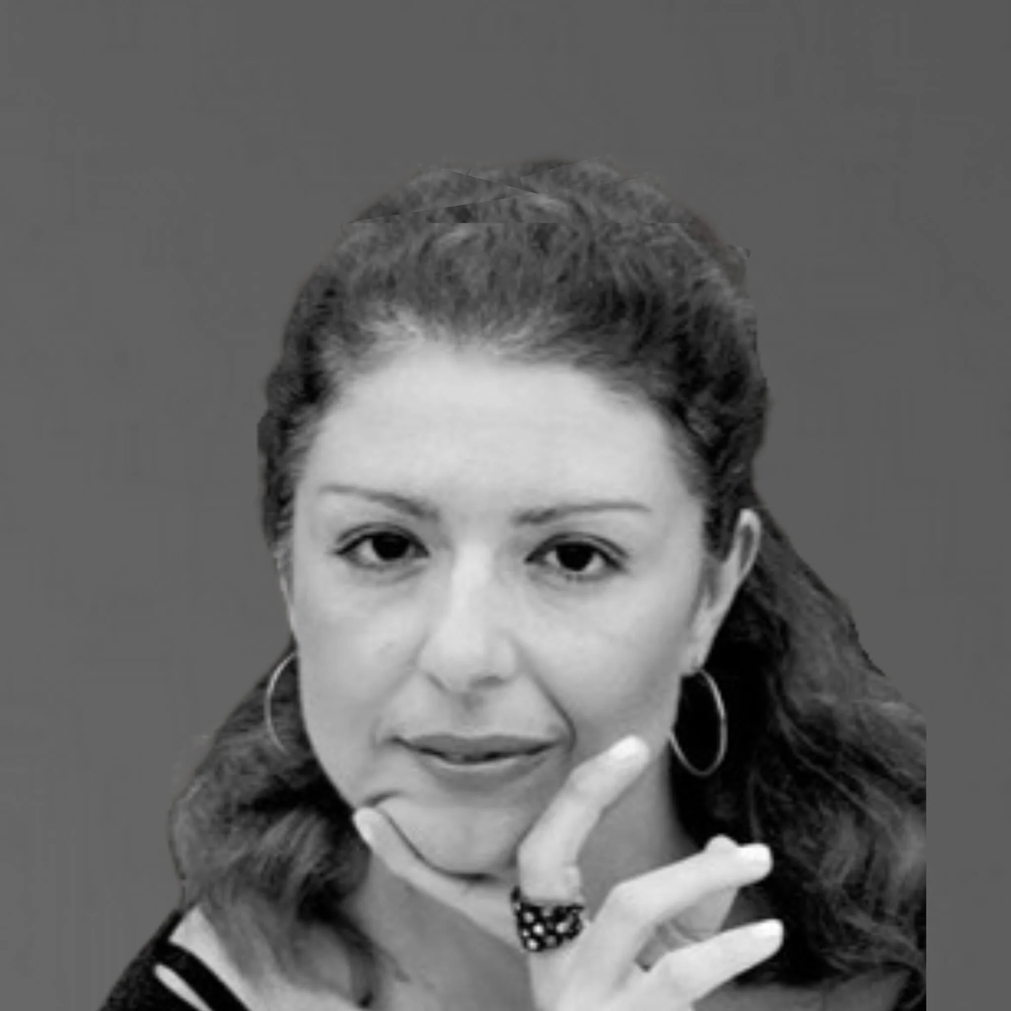 Black and white portrait of a woman with wavy hair, wearing hoop earrings and a ring, with her hand near her chin, against a plain background.