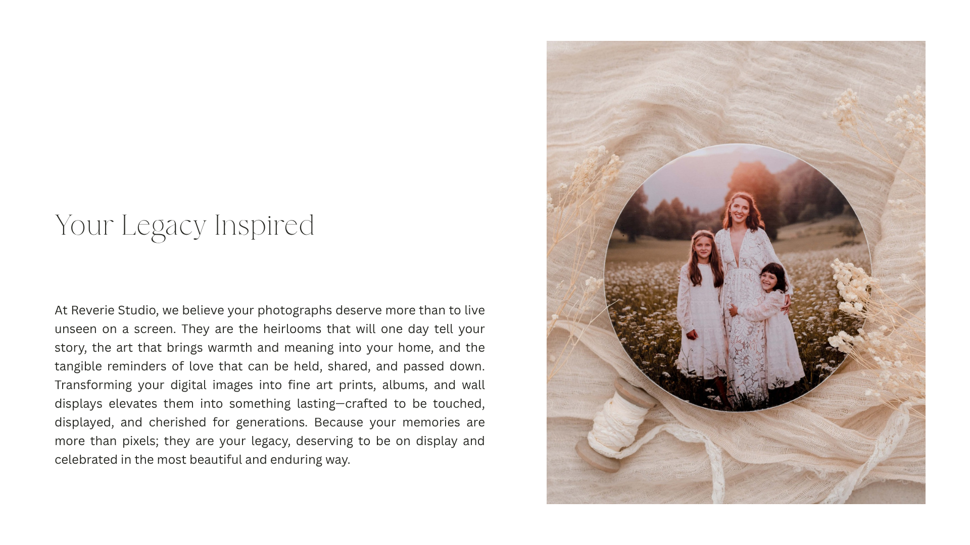 A round wooden photo of a woman and two girls in white dresses, standing in a field of white flowers during sunset, placed on a beige fabric backdrop with dried flowers.