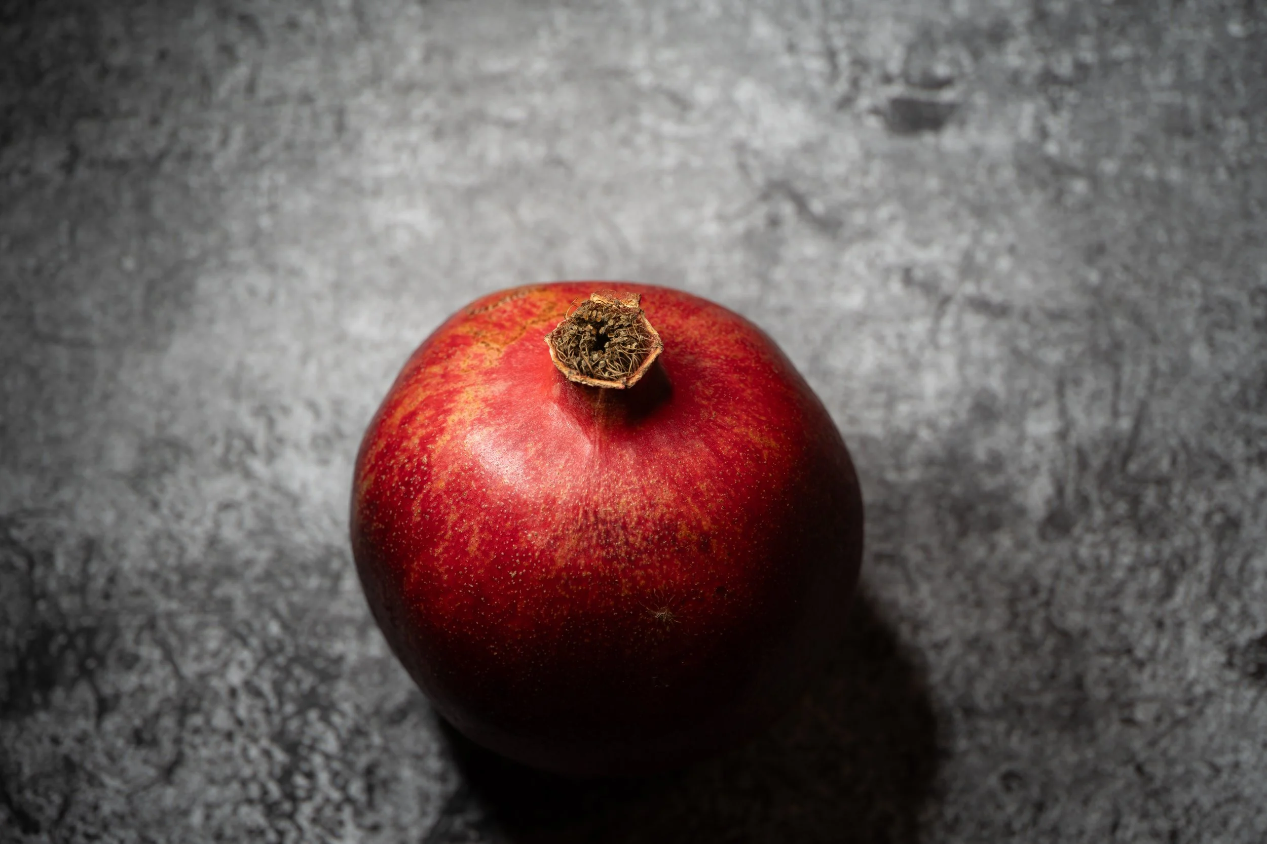 Red pomegranate on gray surface. Copyright Photography - Christoph Rutenkolk