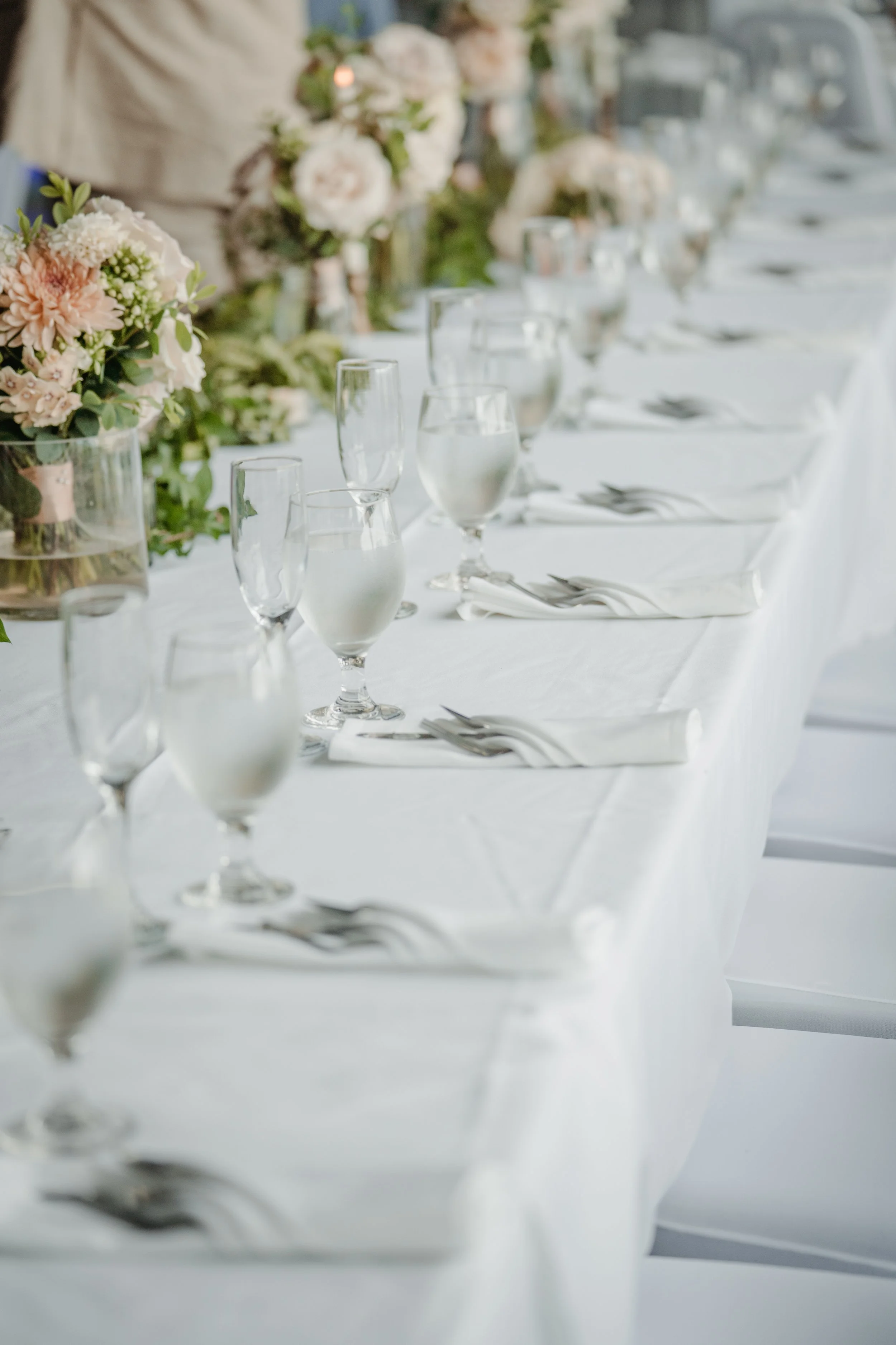 Wedding table scape featuring blush florals, glassware, utensils, and napkins