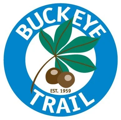 Logo with a blue circle background, featuring a green leaf, two brown berries, and the text "BUCKEYE TRAIL EST. 1959".