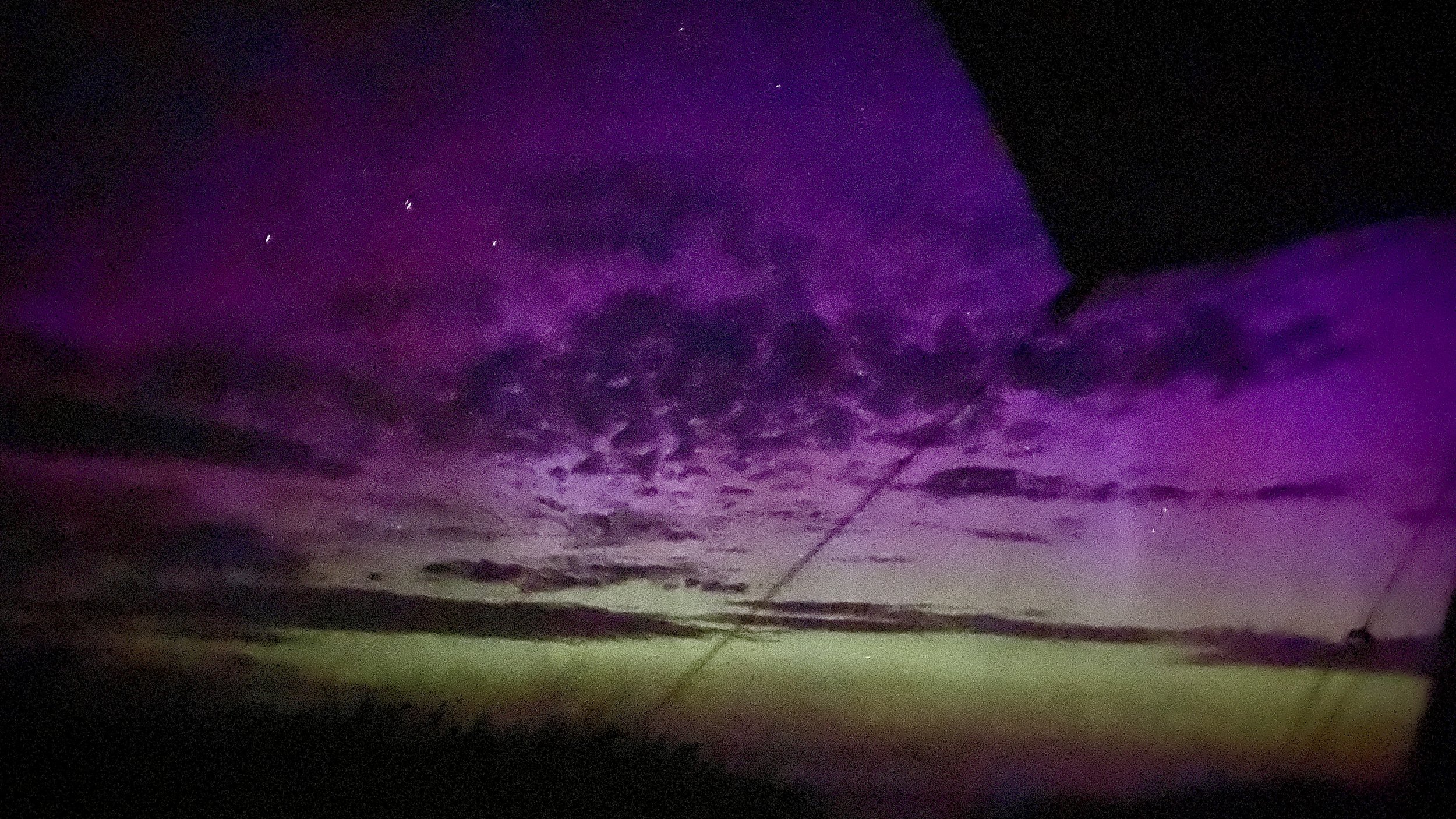 Purple and green colored sky at night, possibly the Northern Lights (Aurora Borealis), with some clouds and faint stars visible.